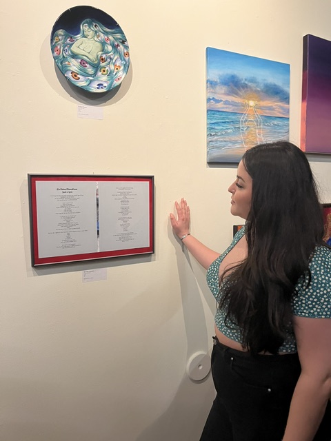 Woman with long dark hair looking at framed document on wall, with colorful artwork and decorative plate nearby.