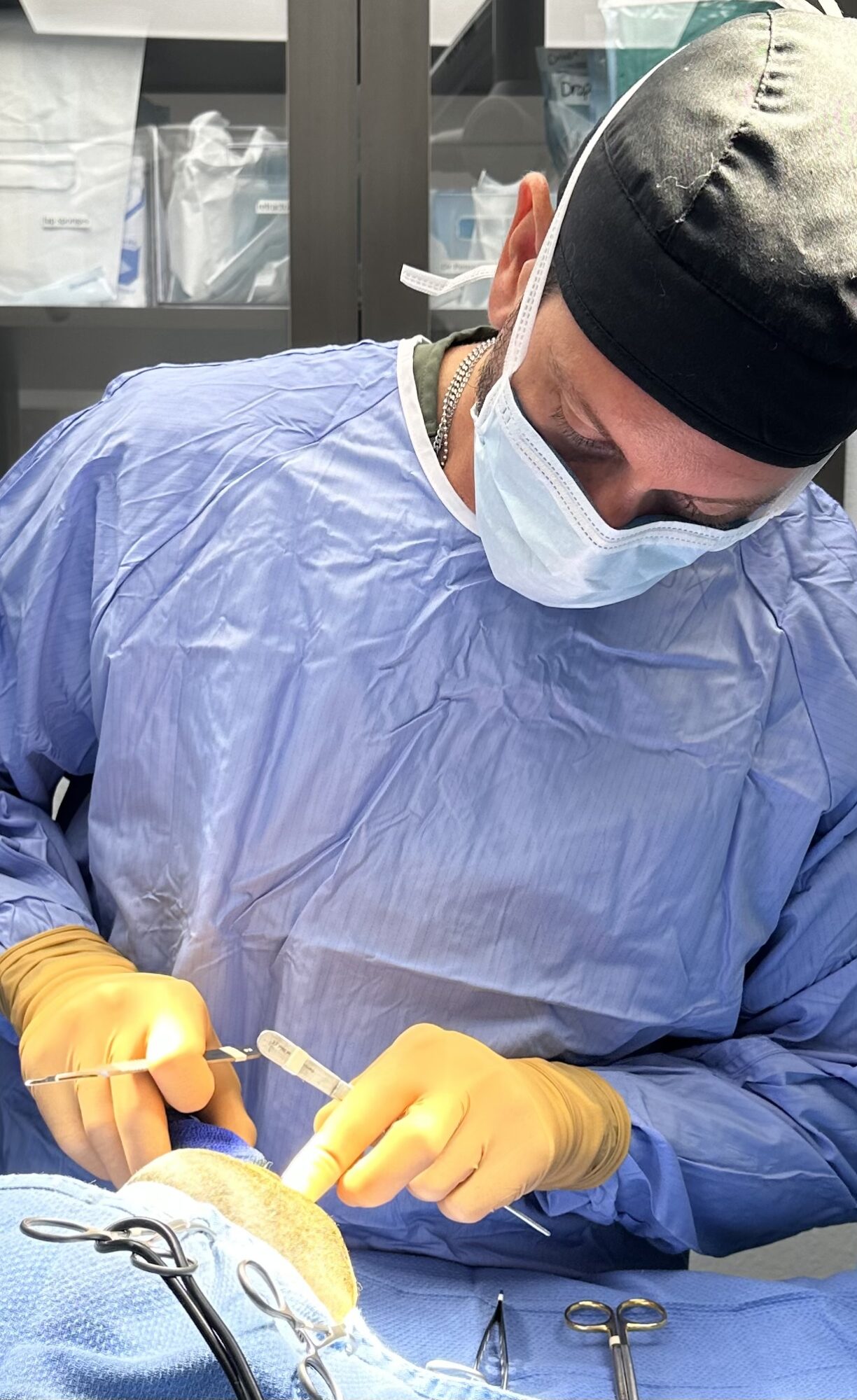 Medical professional in scrubs, mask, and gloves performing a procedure in a clinical setting.
