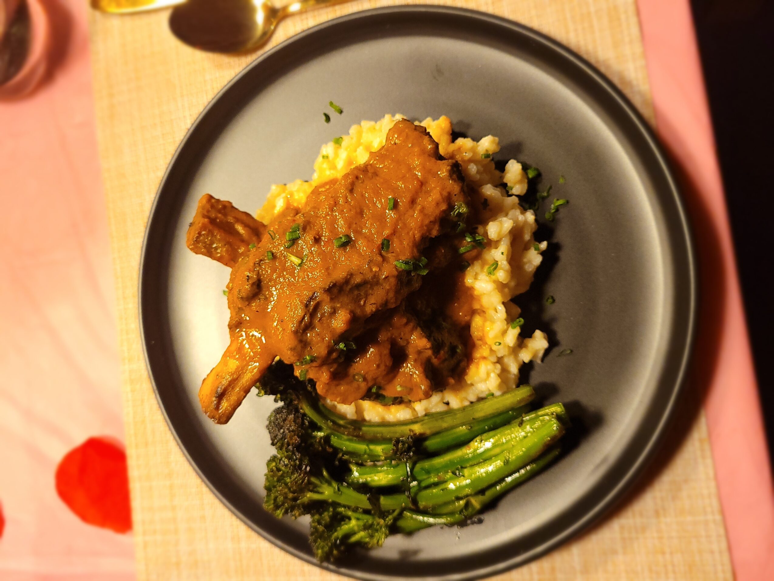 A plate with a piece of meat with sauce, mashed potatoes, and green vegetables on a black plate.