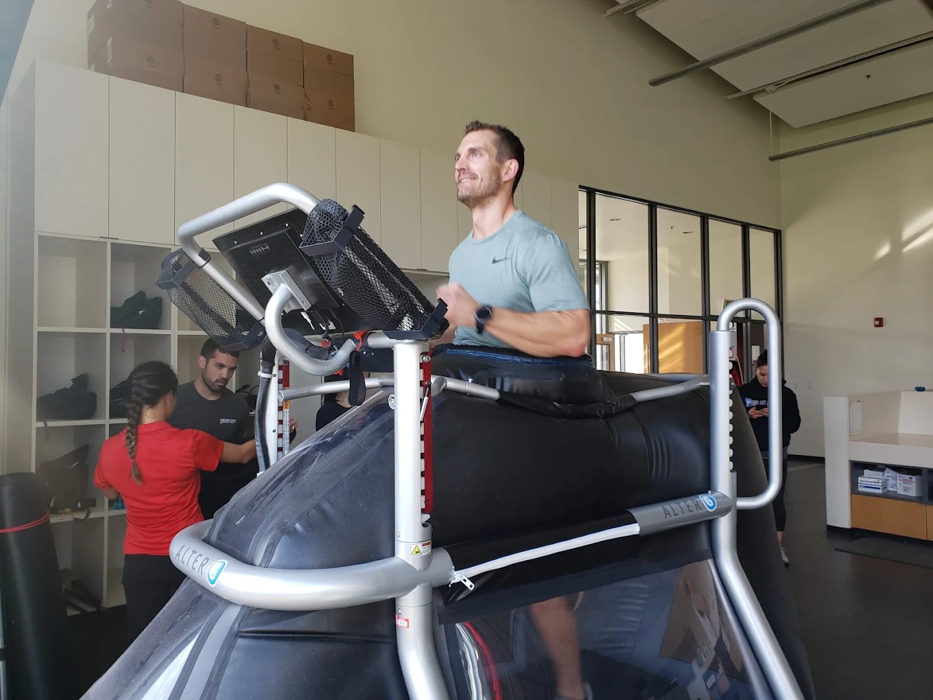 Man walking on a treadmill in a gym with other people in the background.