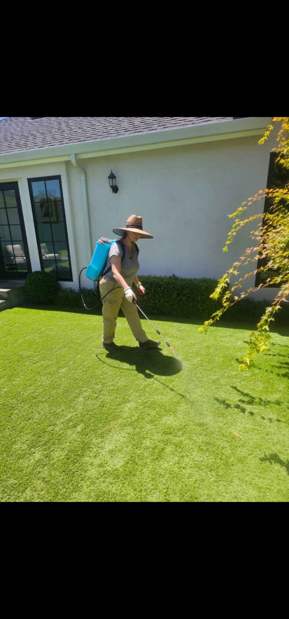 Person wearing a hat and backpack walking on a green lawn near a white house with a sliding door.