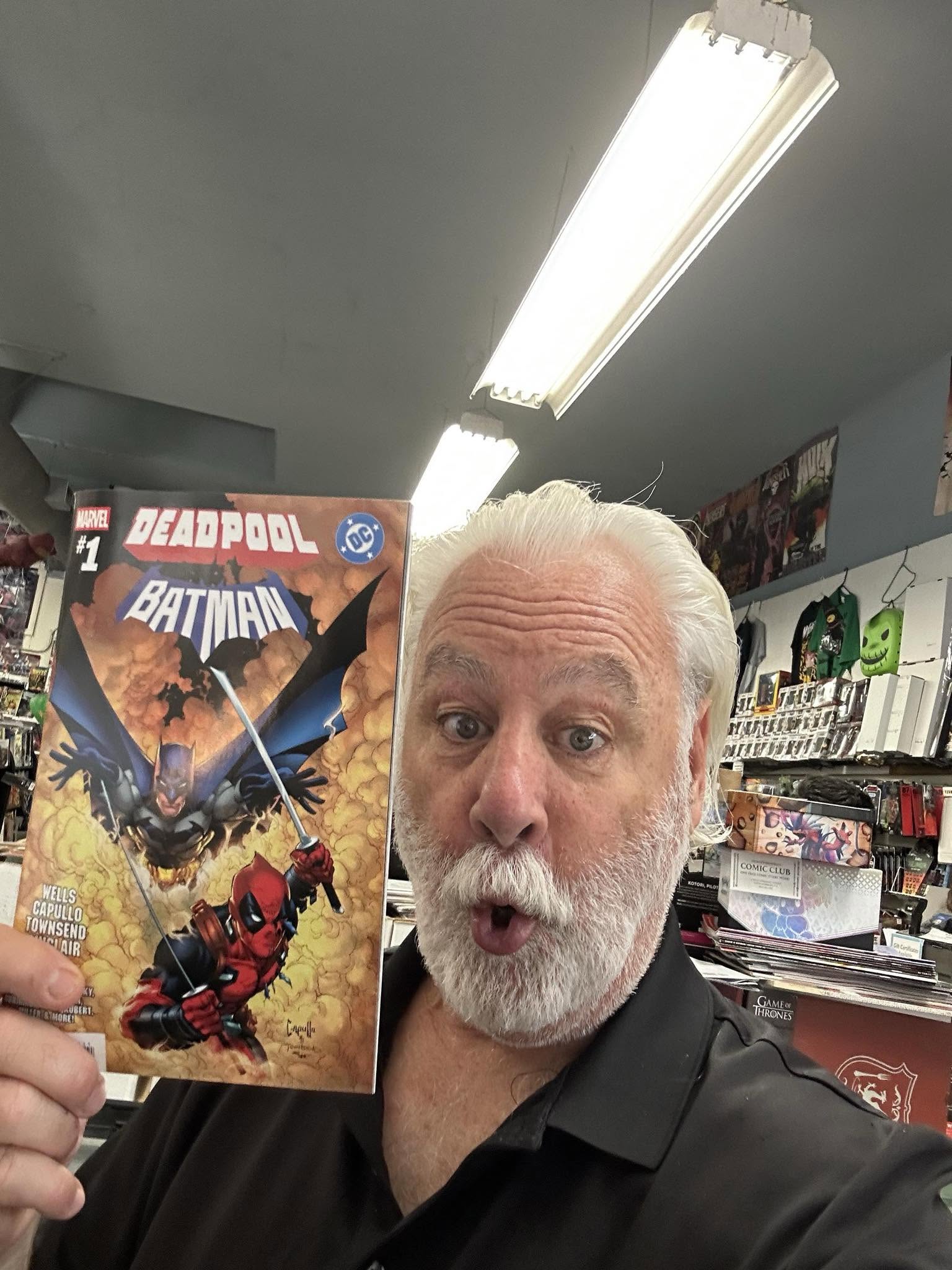 Older man with white hair and beard holding a Deadpool comic book, surprised expression, store interior with shelves and bright ceiling lights