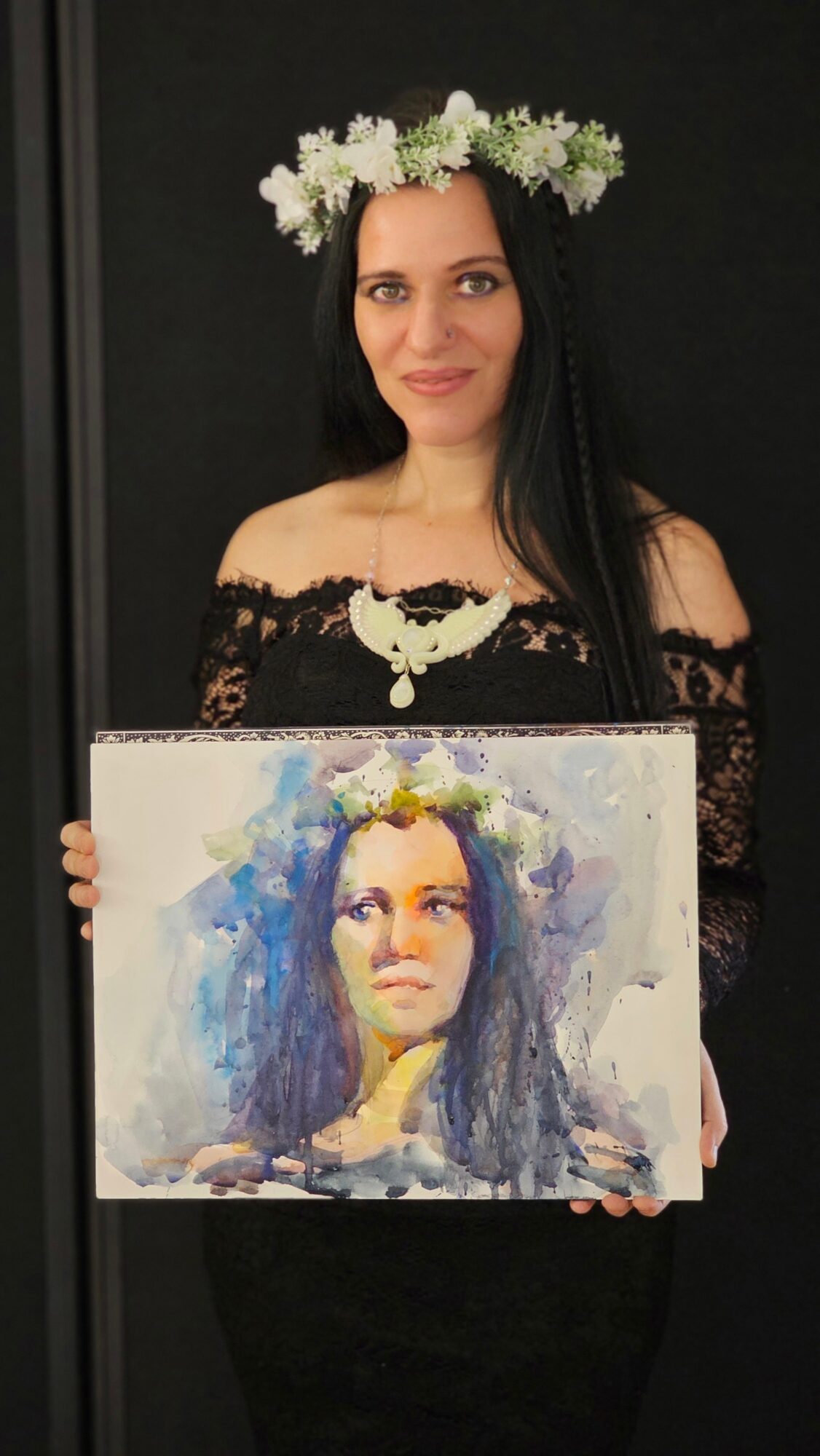 Woman with a flower crown holding a painting of herself, wearing an off-shoulder black dress, against a dark background.