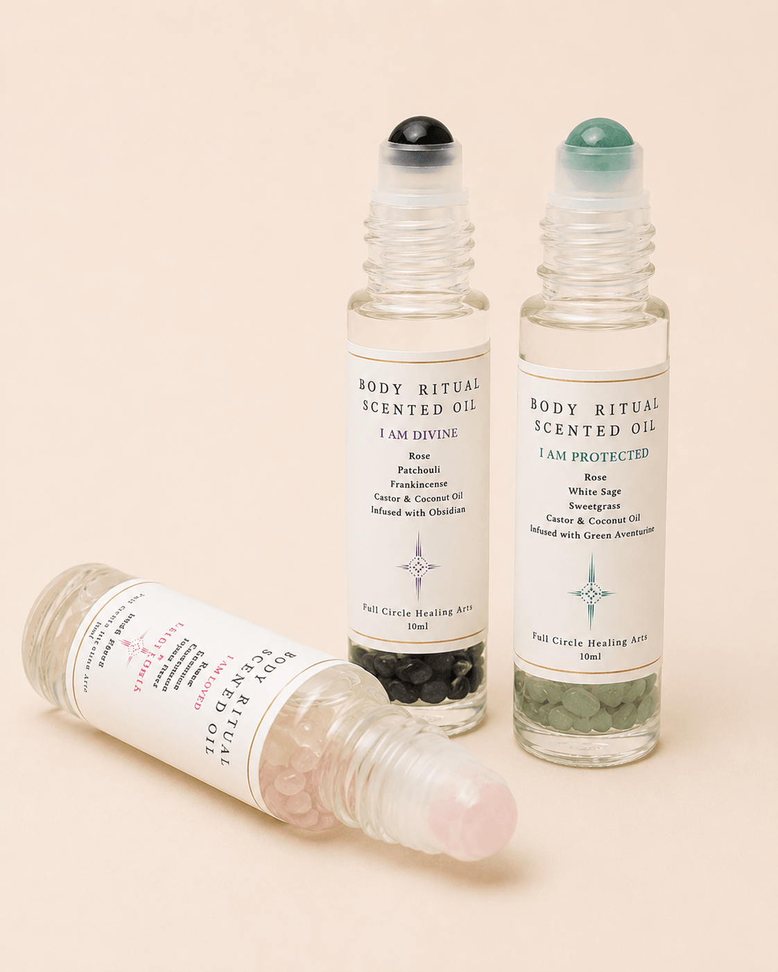Three transparent bottles with black, green, and pink caps, labeled as scented oils, standing upright and one lying down.