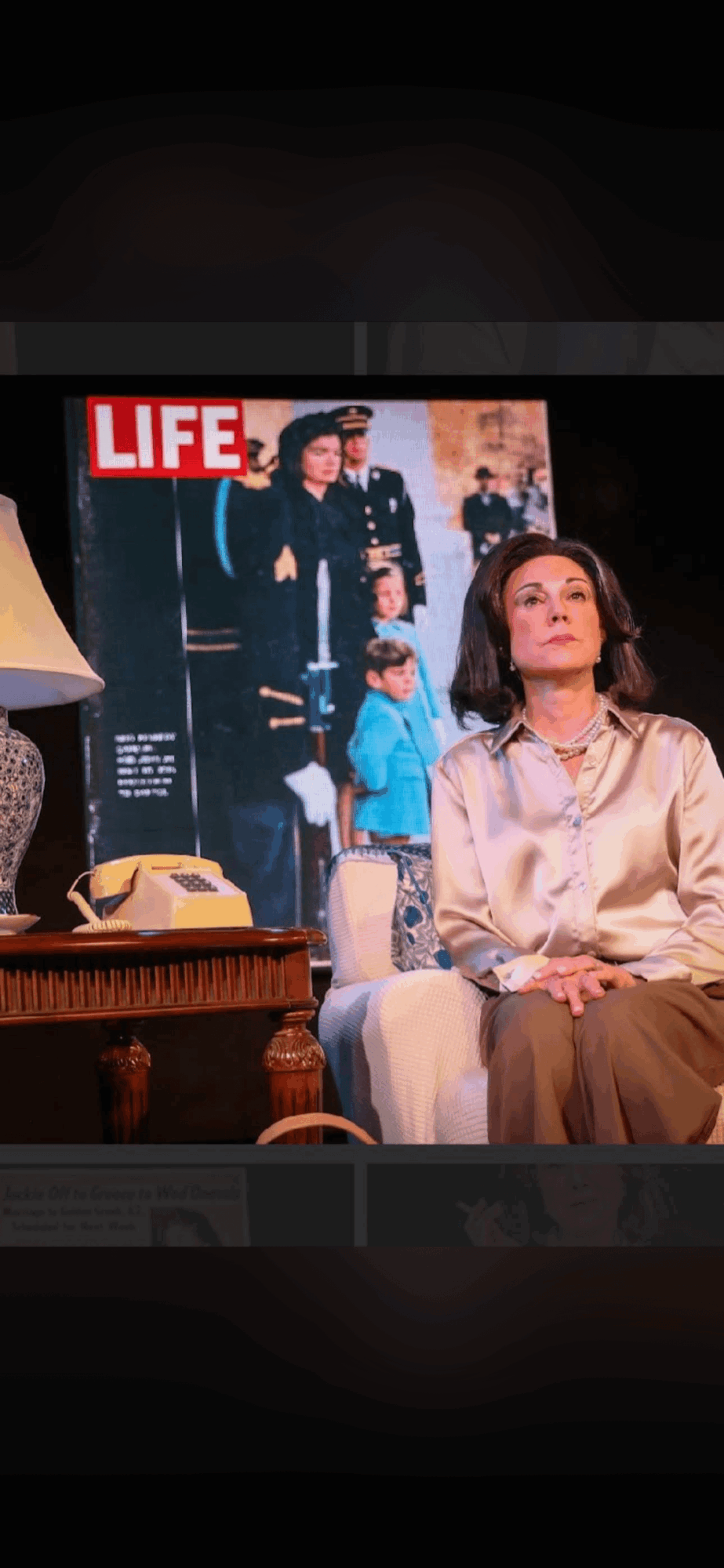 Woman sitting on a couch in a room with a magazine cover on the wall behind her, featuring a group of people and the word 'LIFE'.
