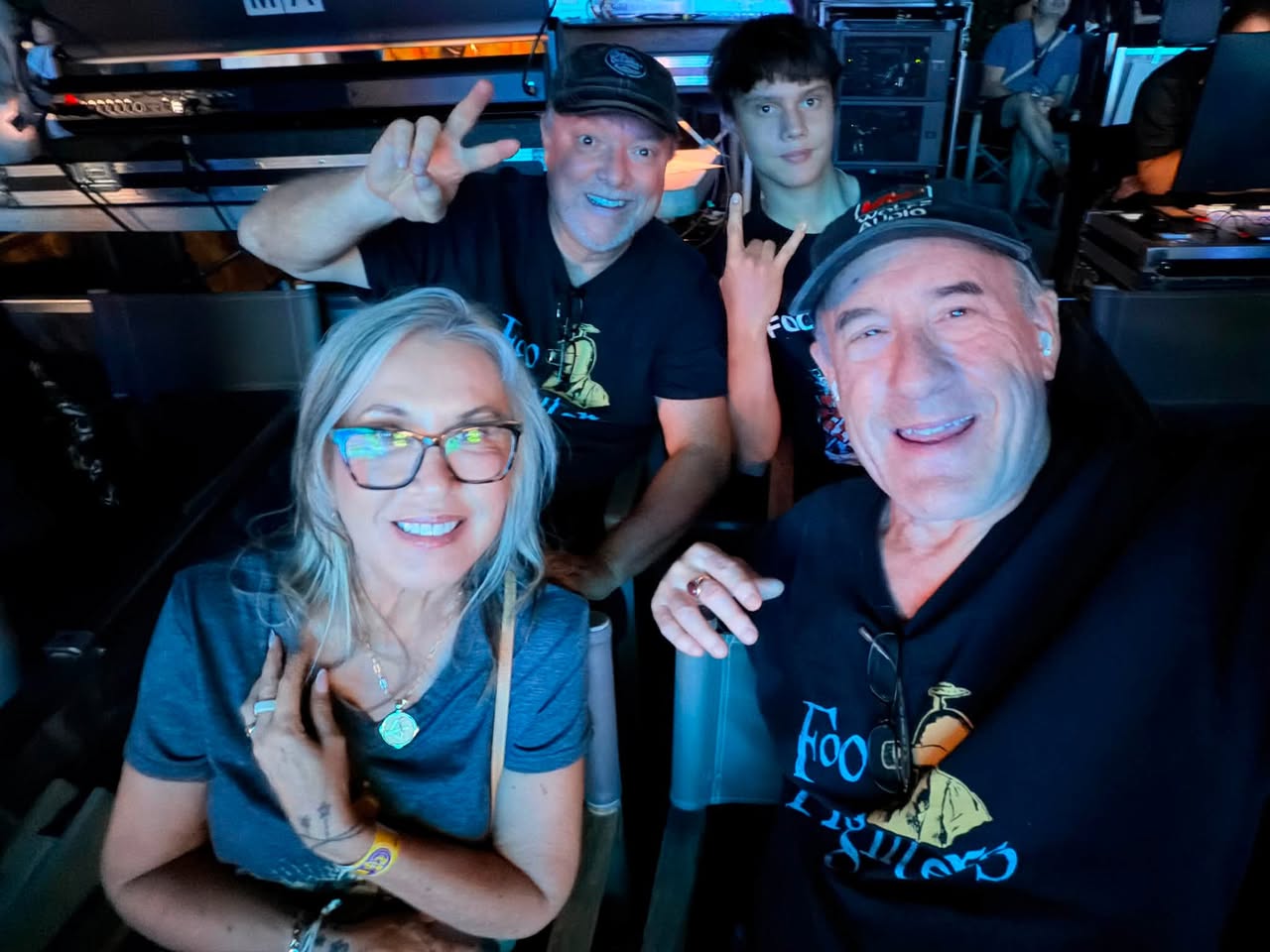 Four people smiling and making peace signs in a room with computer equipment, two in the front and two in the back.