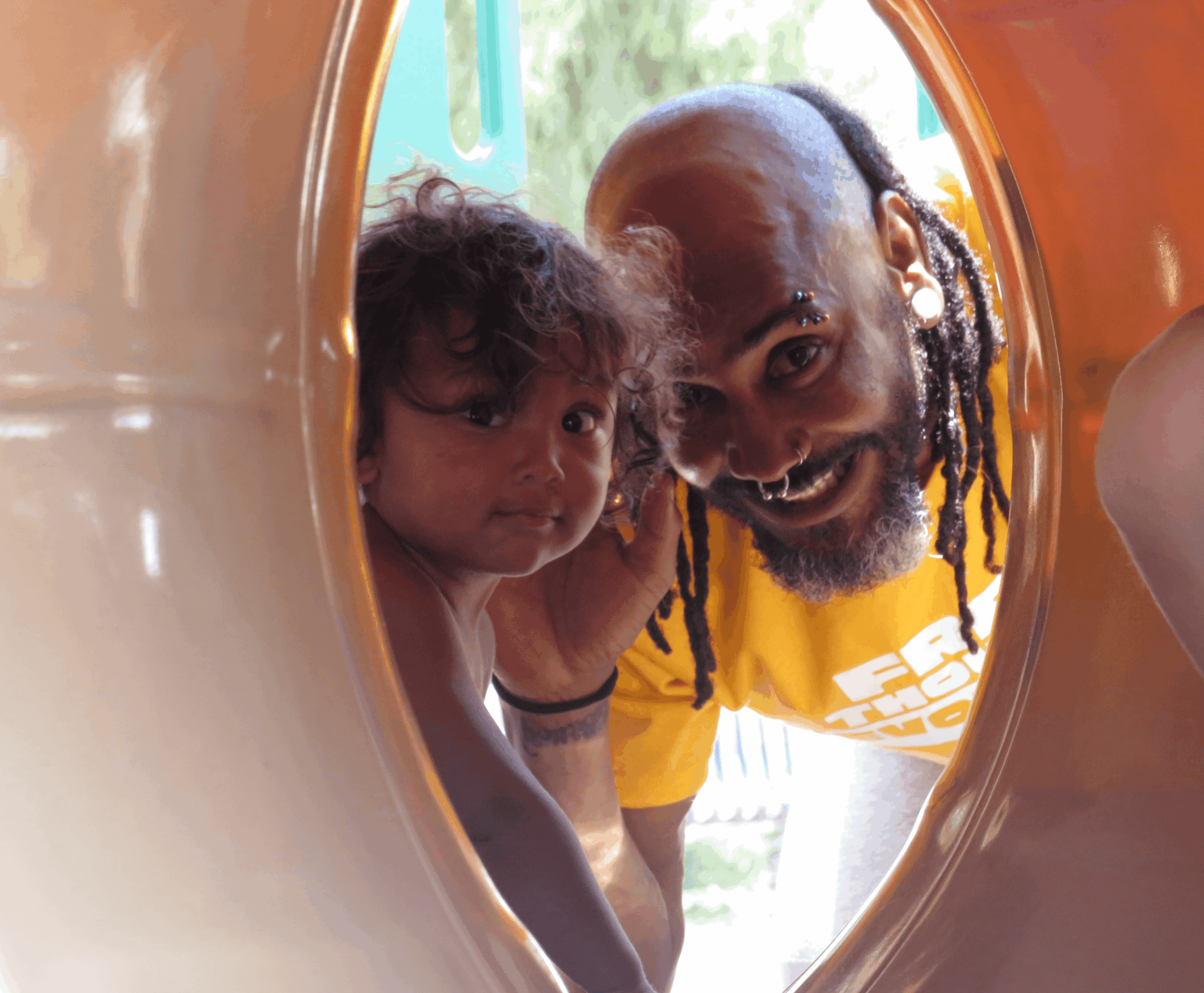Man and child looking through a circular opening, smiling, with colorful play equipment around them.