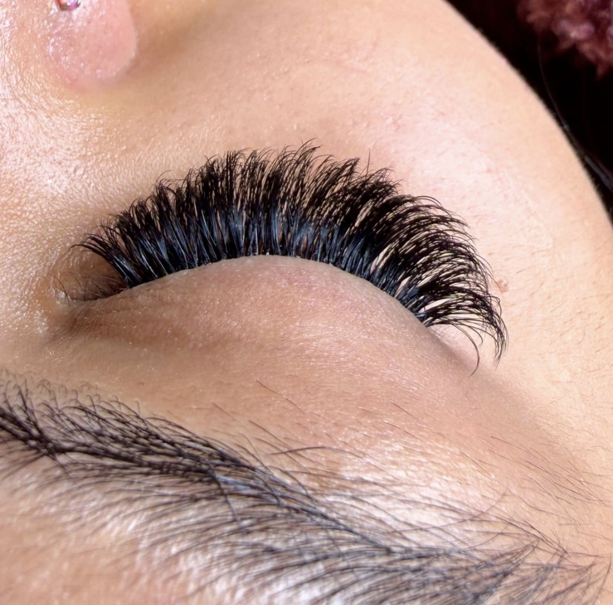 Close-up of a person's closed eye with long, thick eyelashes and visible skin texture.