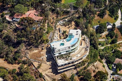Aerial view of a modern multi-story house with a swimming pool on a hillside, surrounded by trees and greenery.
