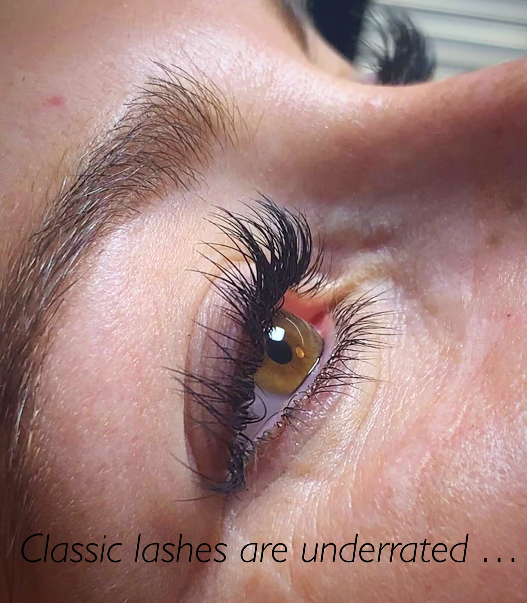 Close-up of a person's eye with long, dark eyelashes and well-groomed eyebrow, looking upward. Text reads: 'Classic lashes are underrated ...'.