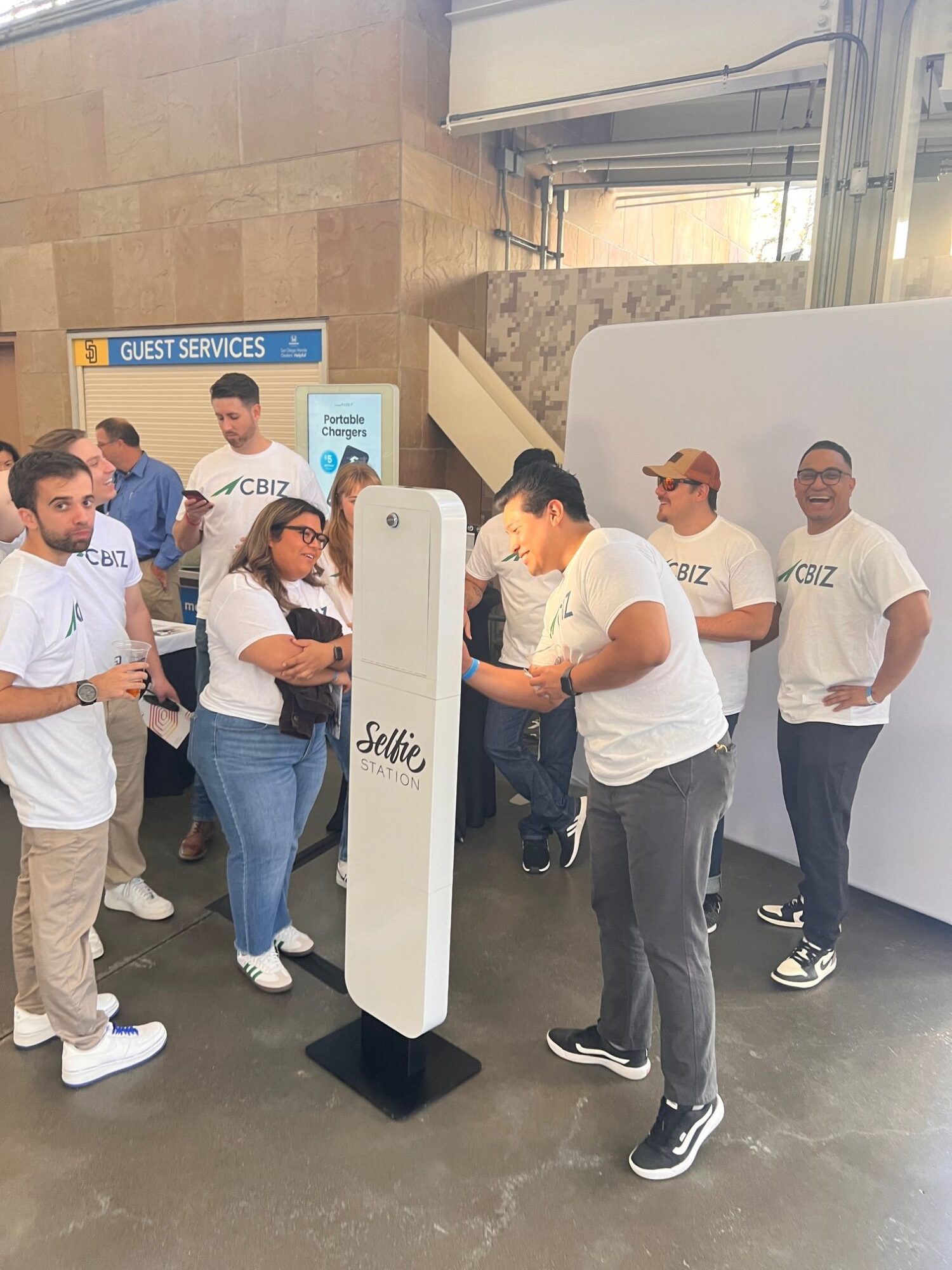 Group of five people standing in a room, some looking at a device, with a white display stand nearby.