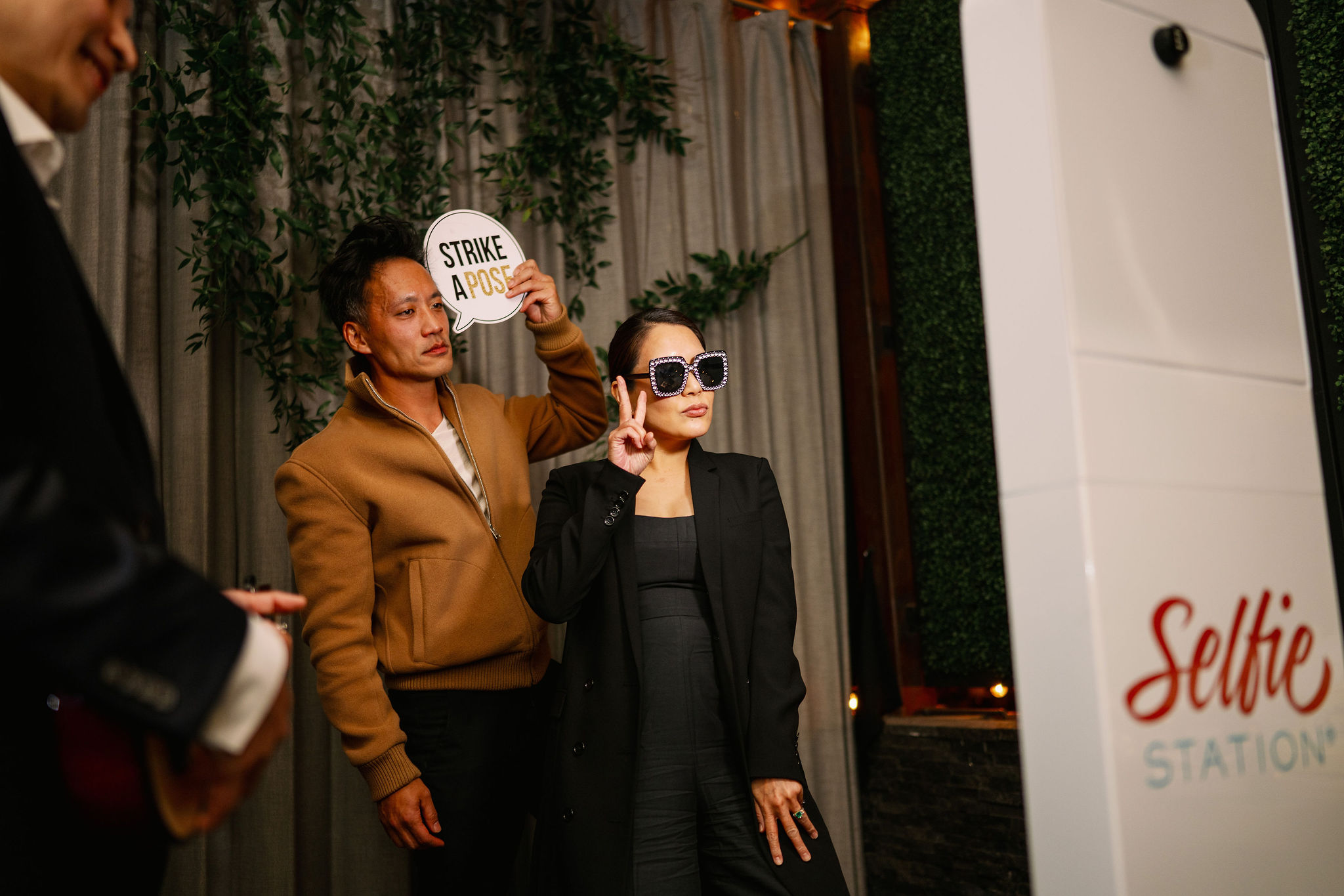 Two women standing outdoors, one holding a sign that says 'STRIKE' and the other wearing sunglasses, with greenery in the background.