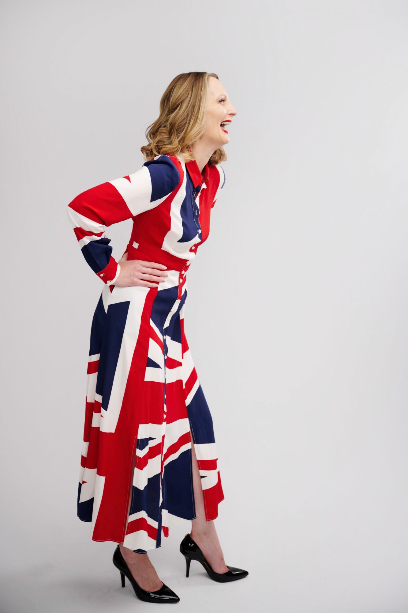 Woman laughing, standing sideways, wearing a dress with a red, white, and blue pattern, and black high heels.