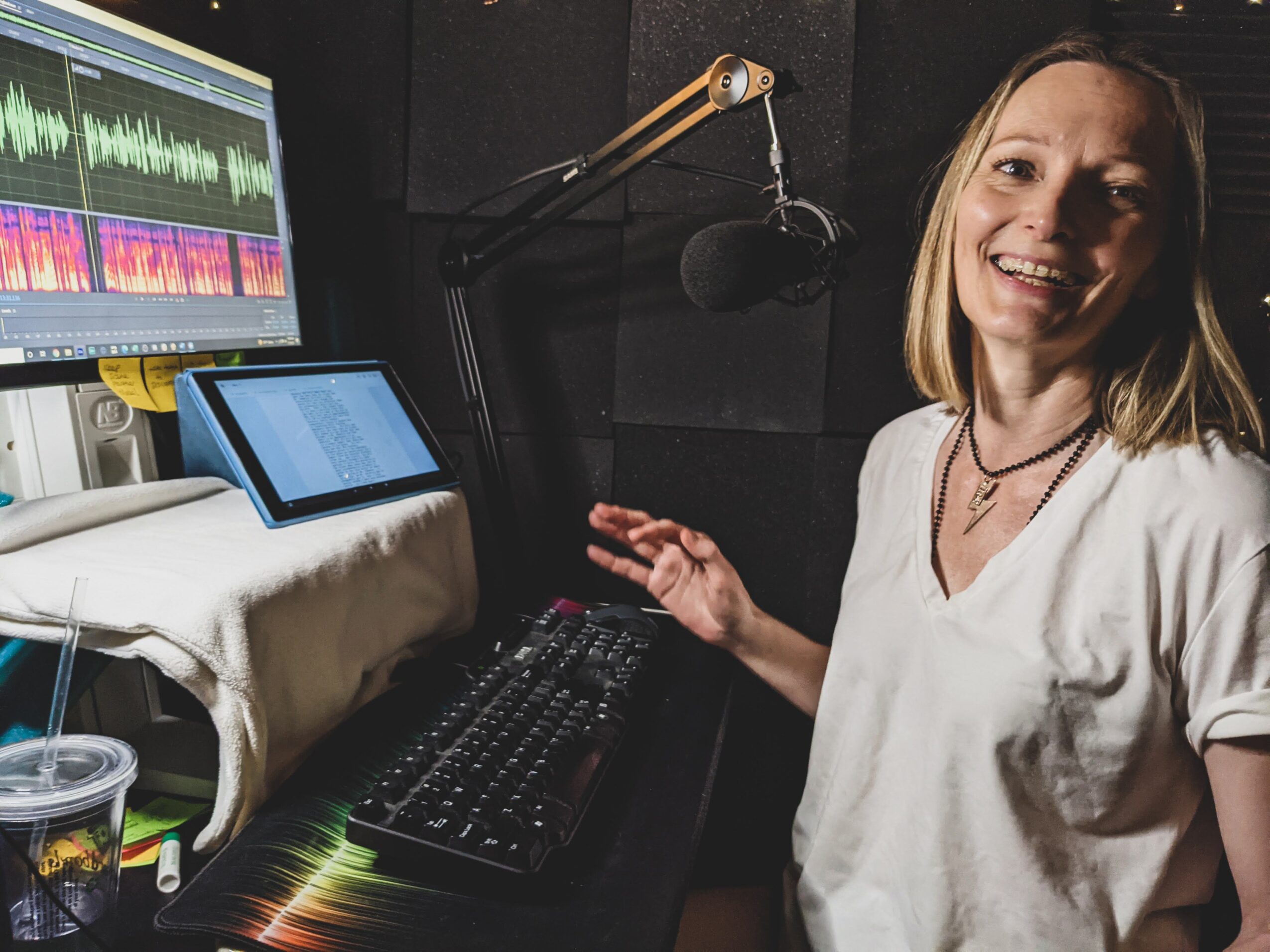 Woman in a recording studio smiling, with audio equipment and a microphone nearby.