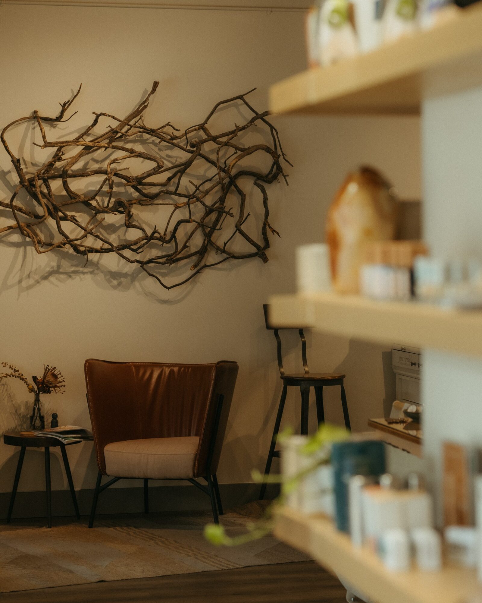 Interior scene with a brown armchair, small side table, and wall art made of intertwined branches, with shelves on the right.