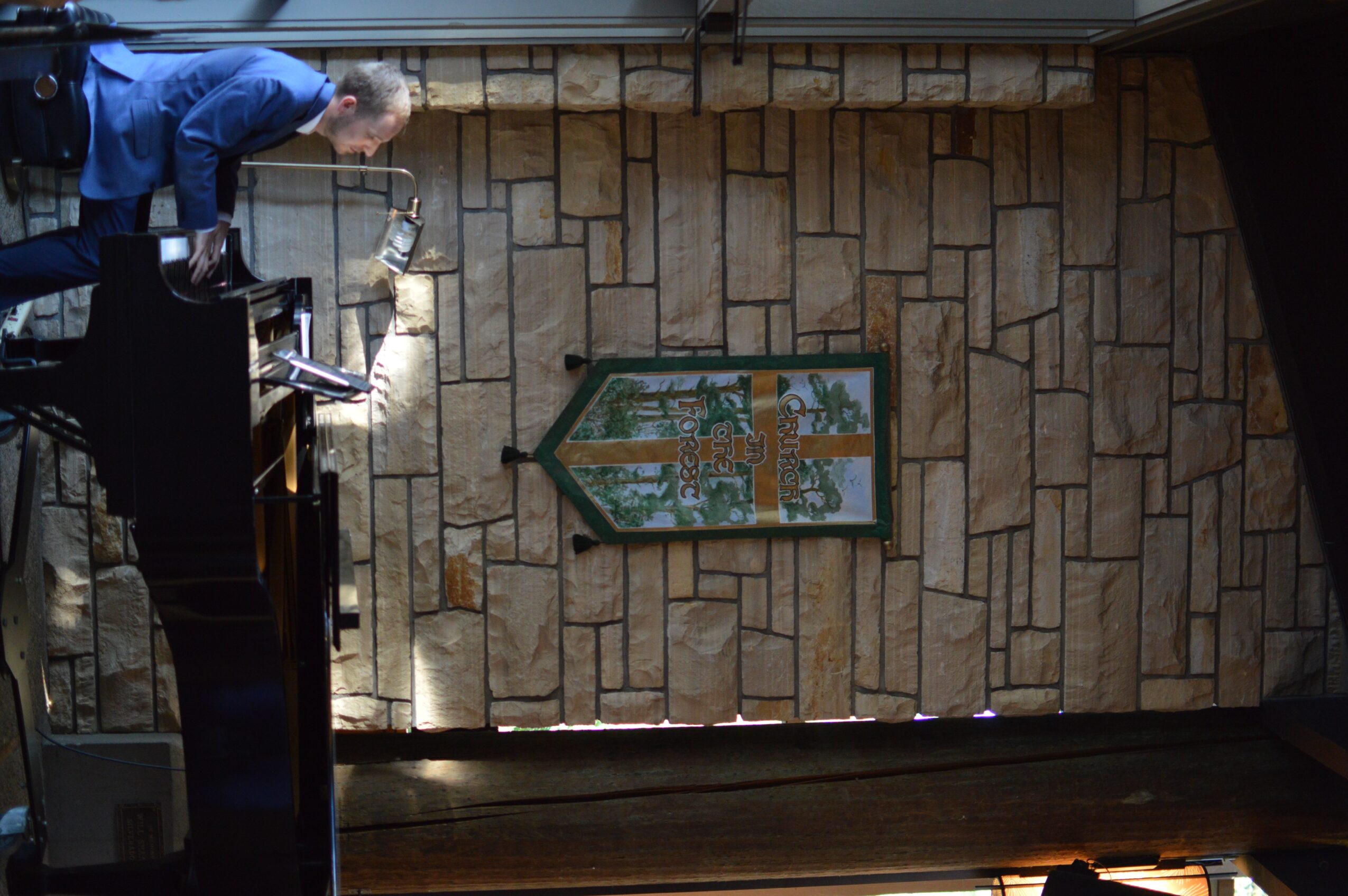 Person standing at a counter with a stone wall and a framed picture behind them, viewed sideways.