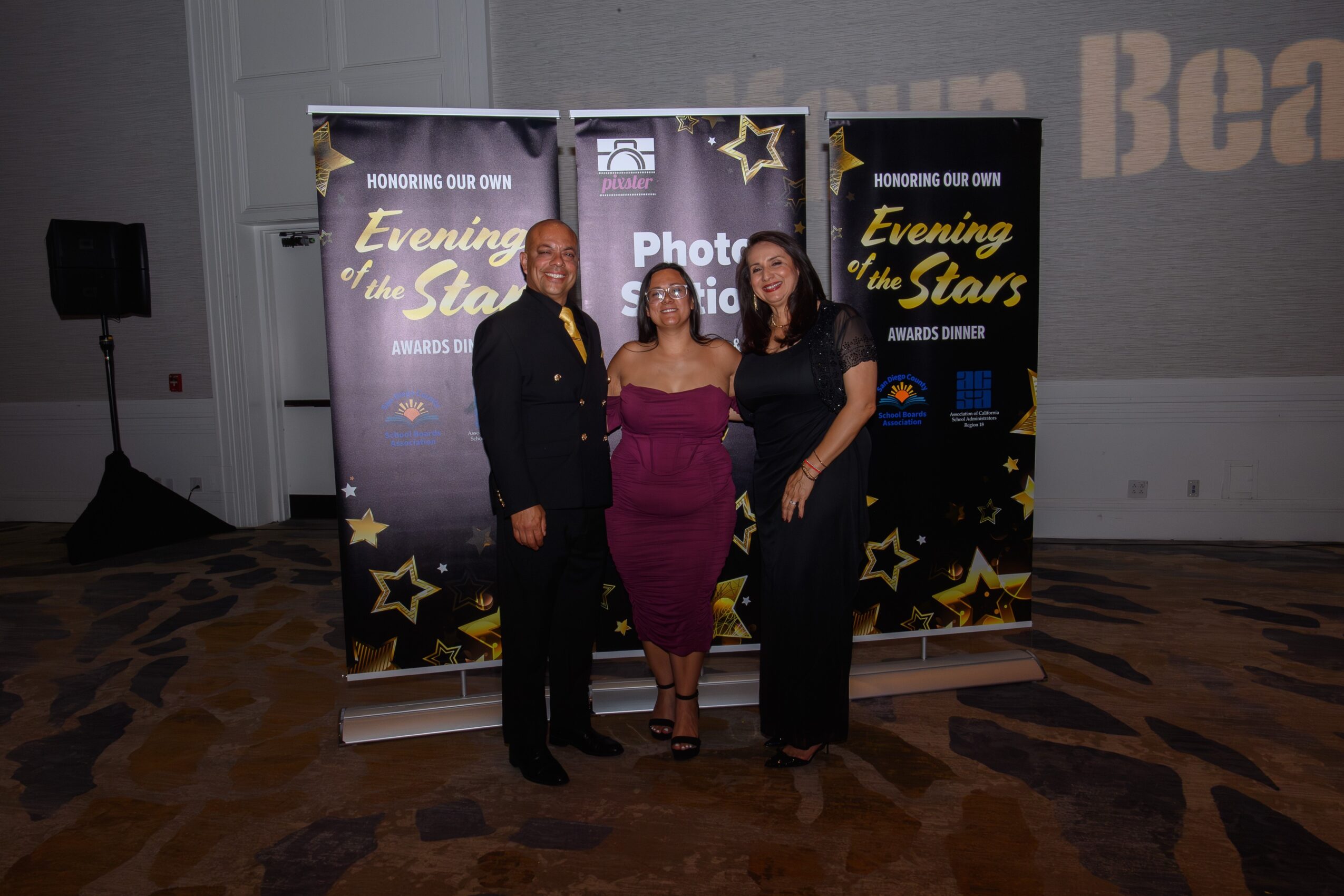 Three people standing in front of a star-themed backdrop at an event, smiling for the photo.