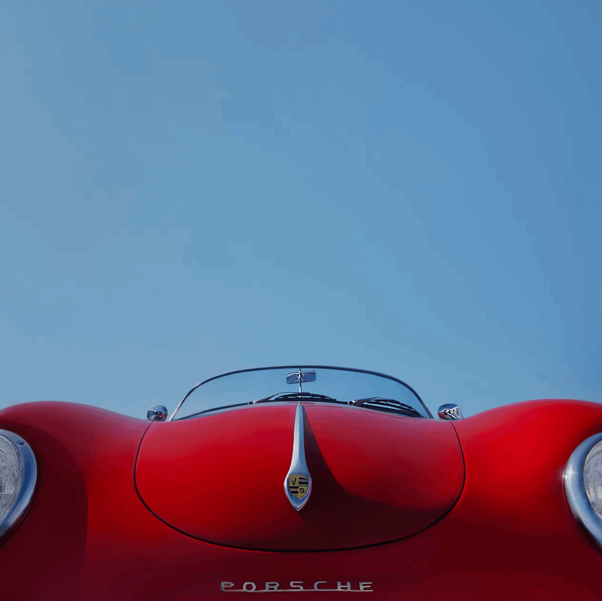 Red Porsche sports car viewed from the front with a clear blue sky background.
