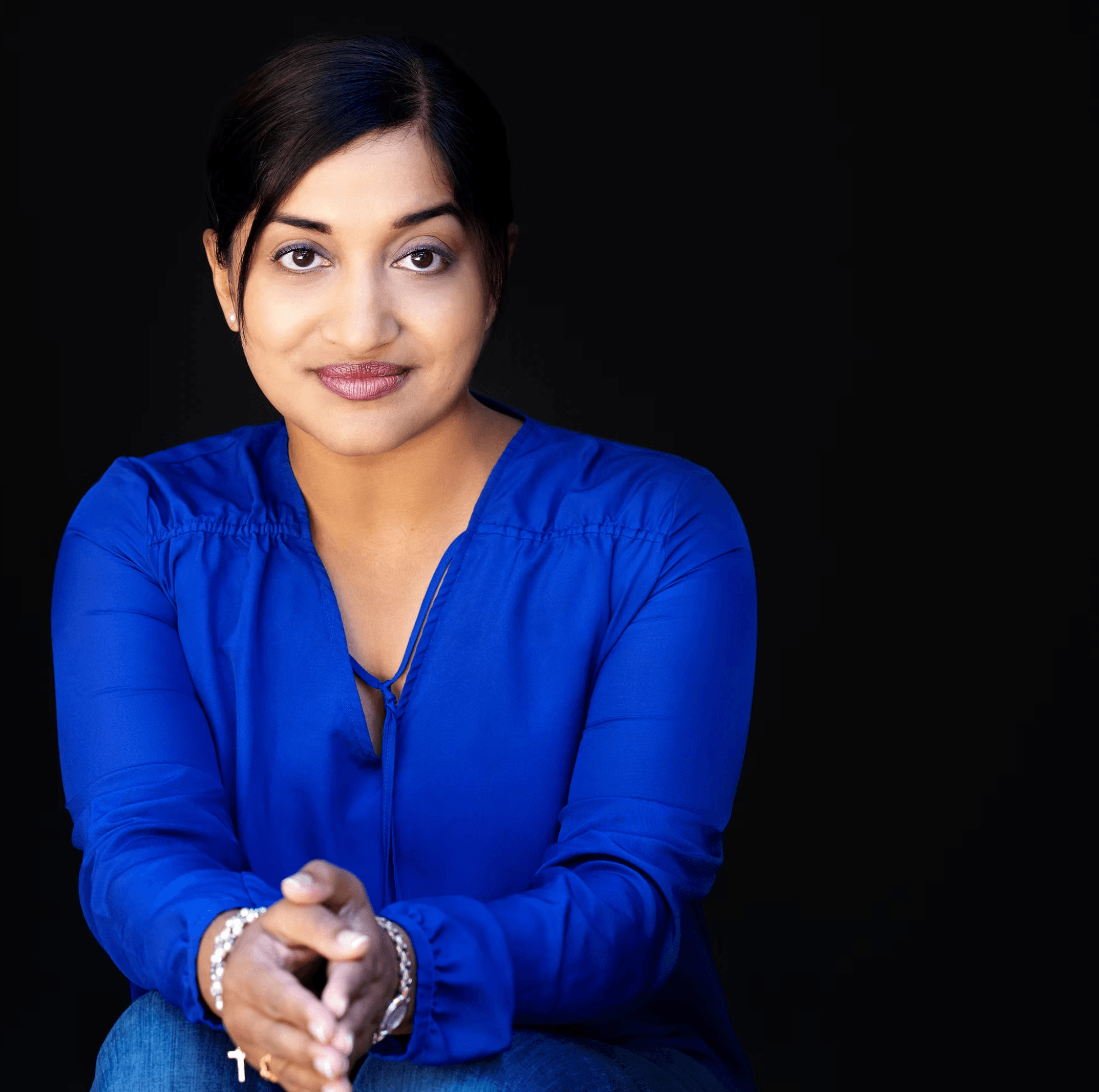 Woman with dark hair in a blue top, smiling, against a black background.