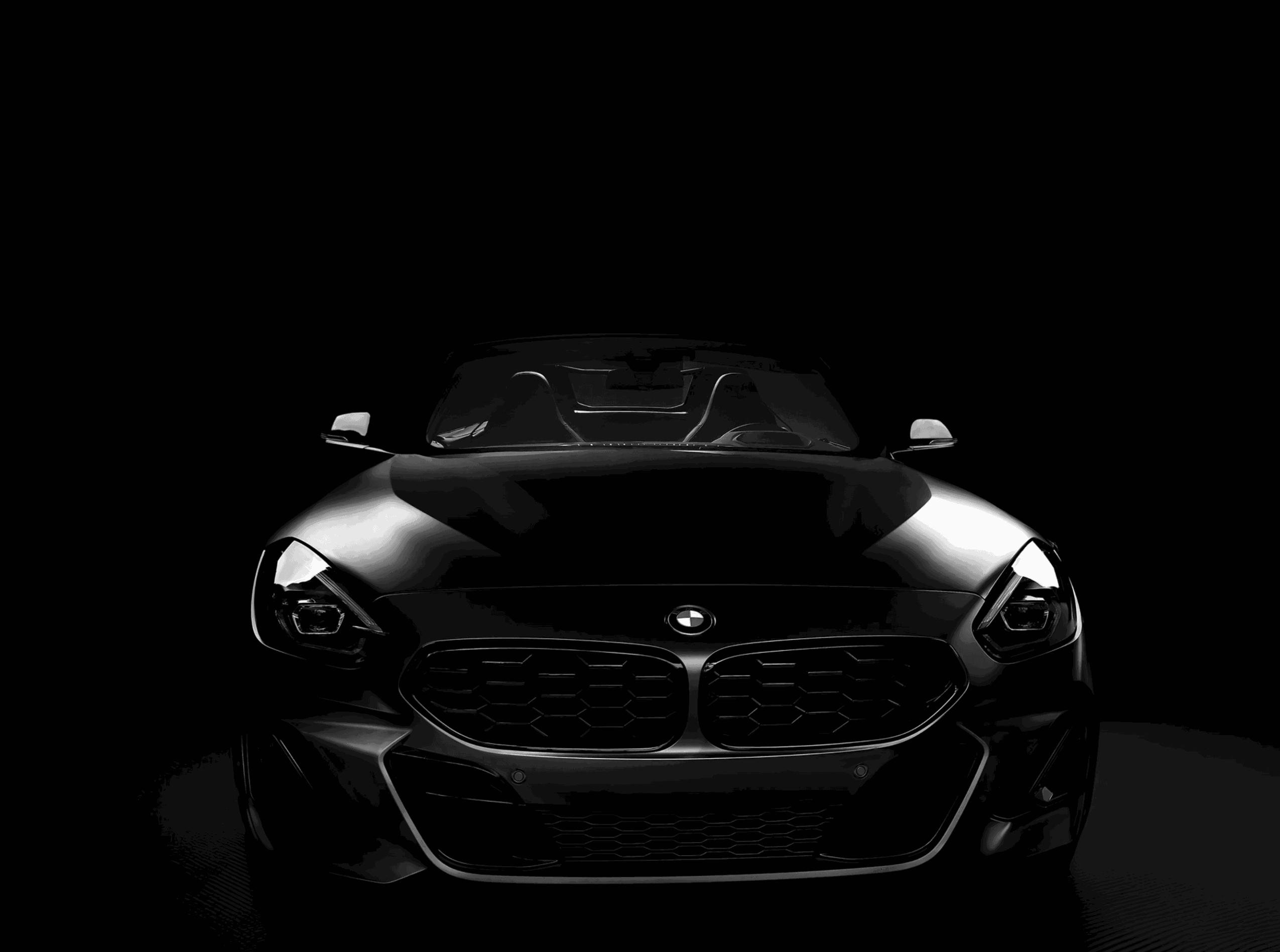 Front view of a sleek black car with illuminated headlights against a dark background.
