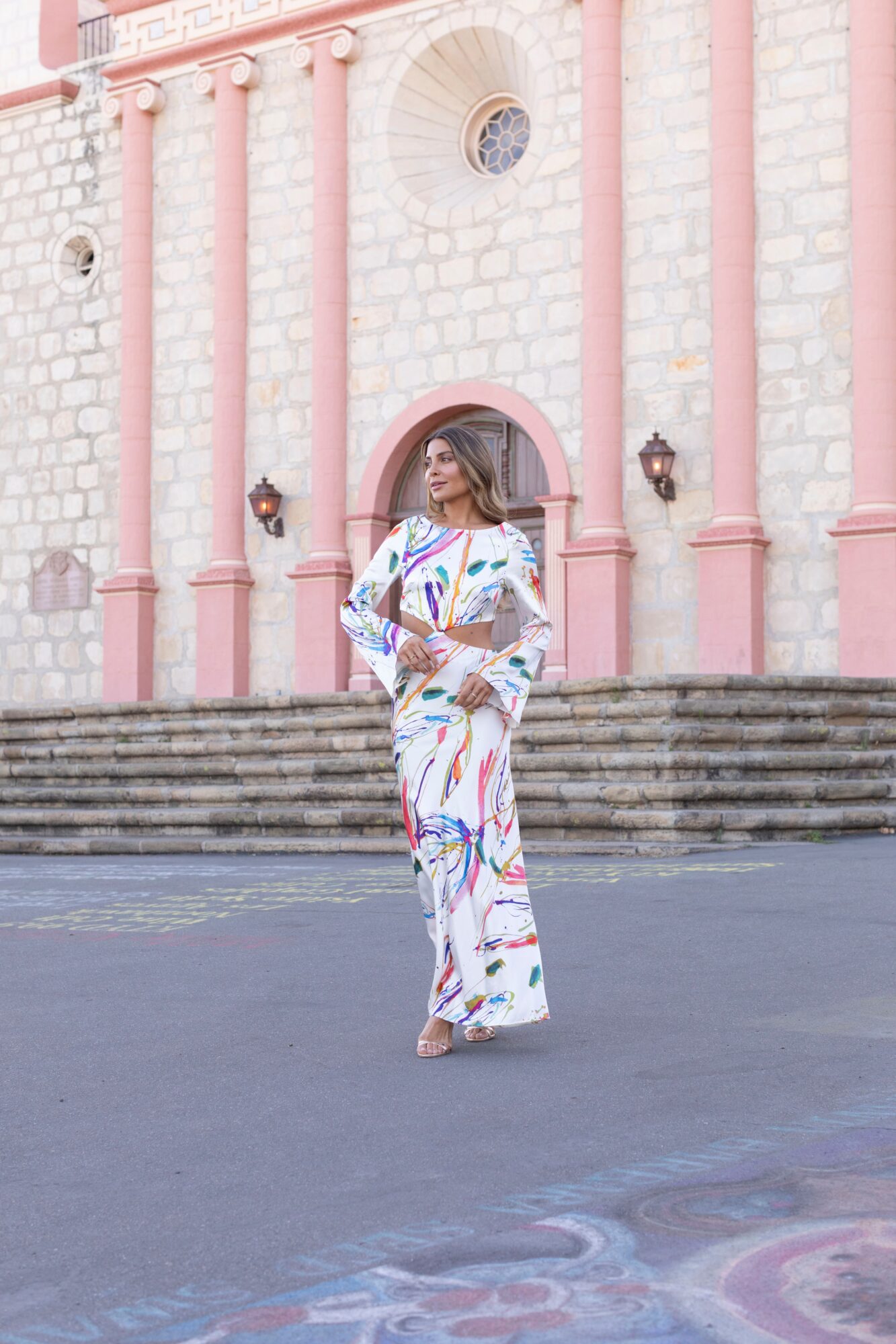 Woman in colorful dress standing in front of a pink and white building with steps and decorative elements.