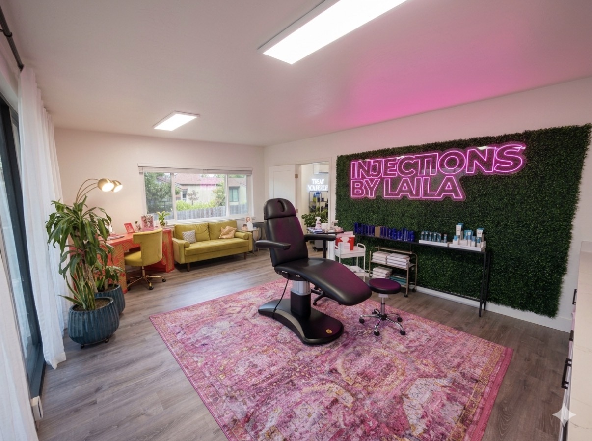 A room with a treatment chair, a pink neon sign, a green wall, and a pink rug, with seating area and plants.
