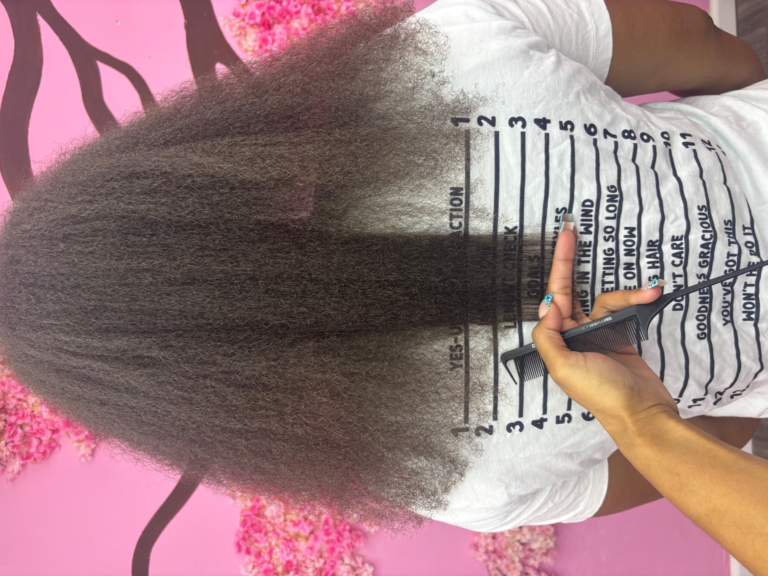 Person with long, straight hair writing on a height chart, pink background, white shirt, hand holding pen.