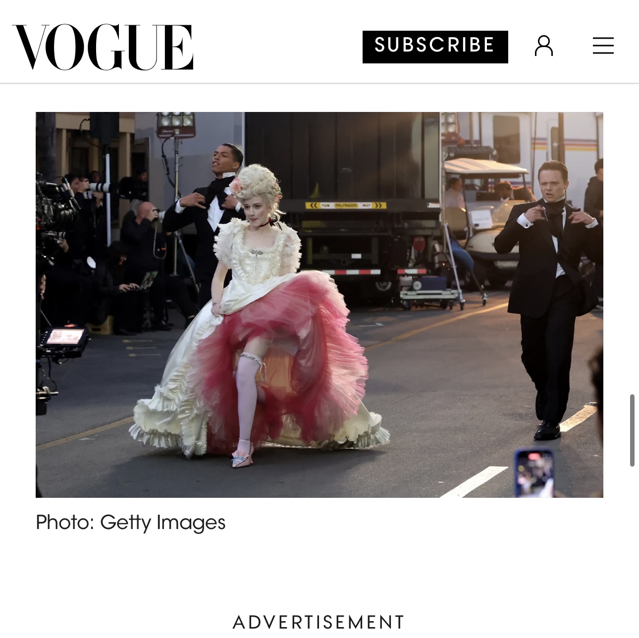 Person in a white dress with a pink tulle skirt walking on a city street, surrounded by photographers and onlookers.