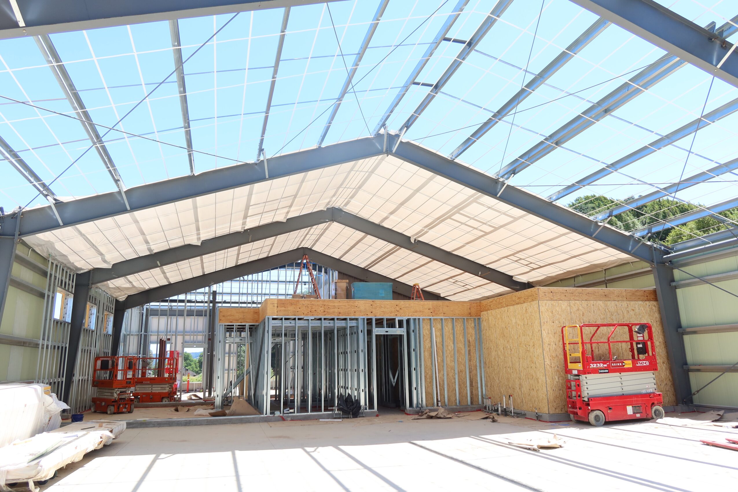 Construction site inside a large building with metal framing and glass ceiling, construction equipment and materials present.