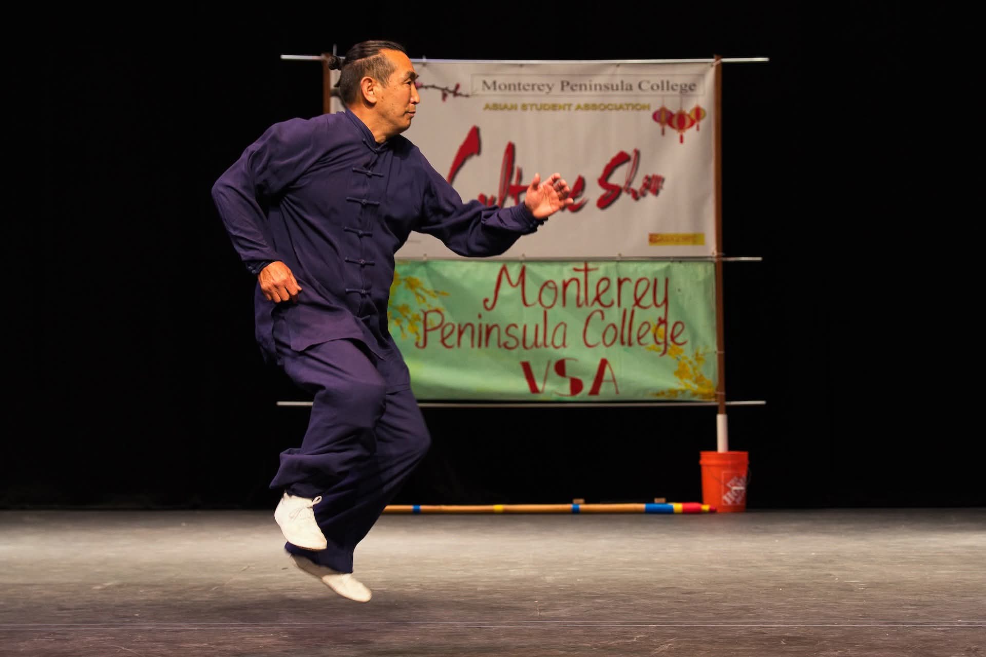 Person performing on stage with a sign reading Monterrey Peninsula College, with a black background.