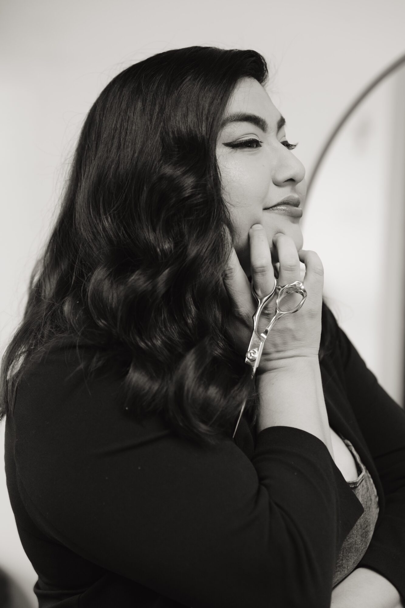 Woman with long wavy hair, eyes closed, touching her face with her hand, in black and white.