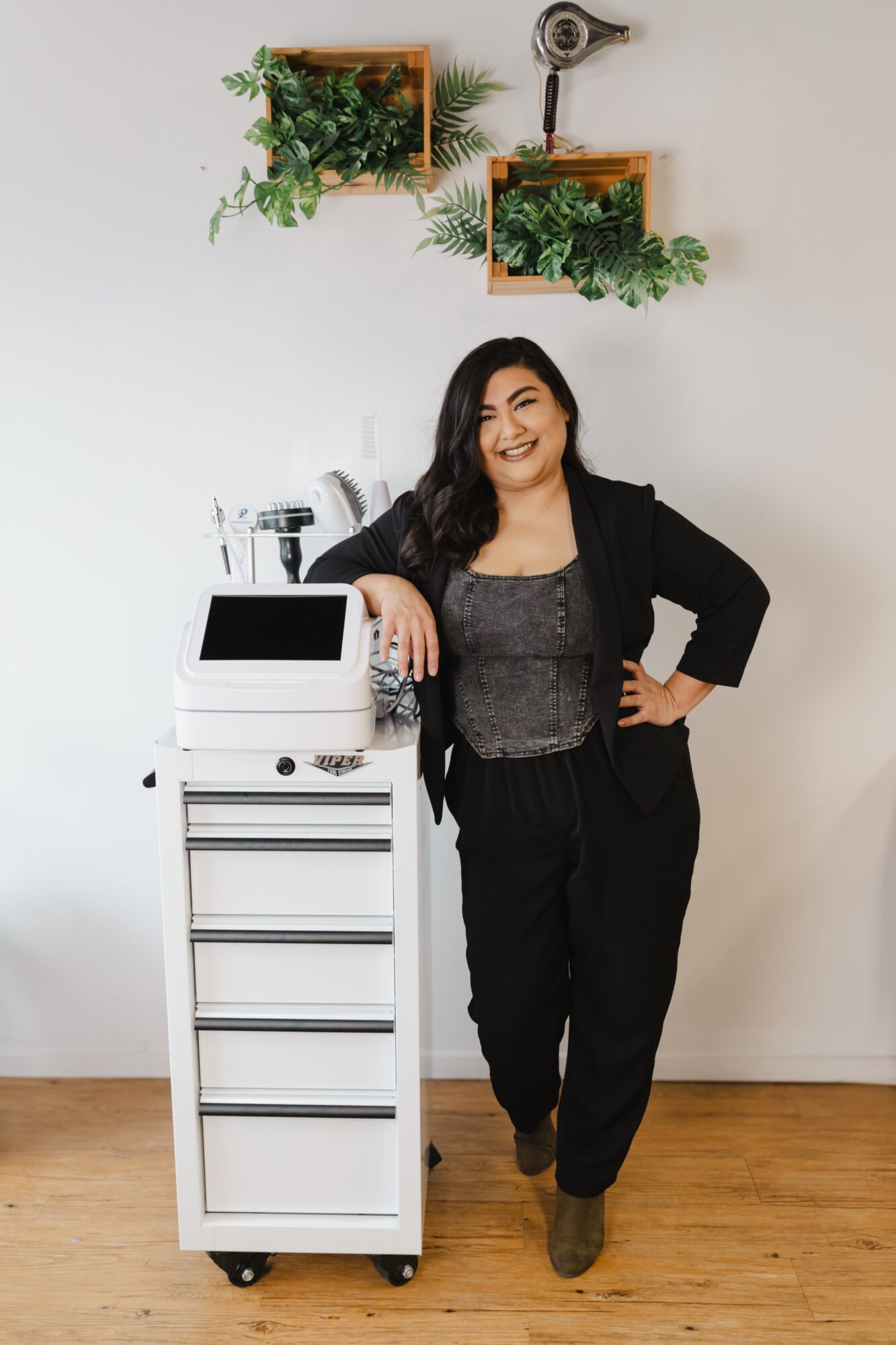 Woman standing next to a white cart with plants and a coffee machine, smiling, in a room with wall-mounted planters.