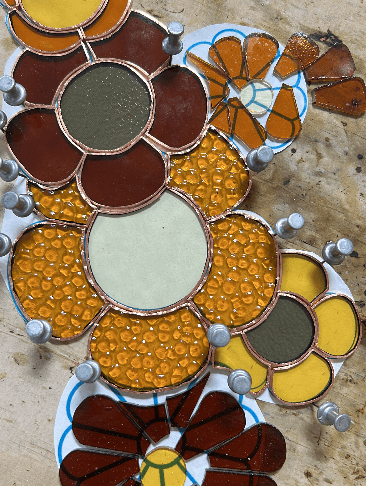 Colorful mosaic with various shapes and textures, including yellow, brown, green, and orange elements, on a stone surface.
