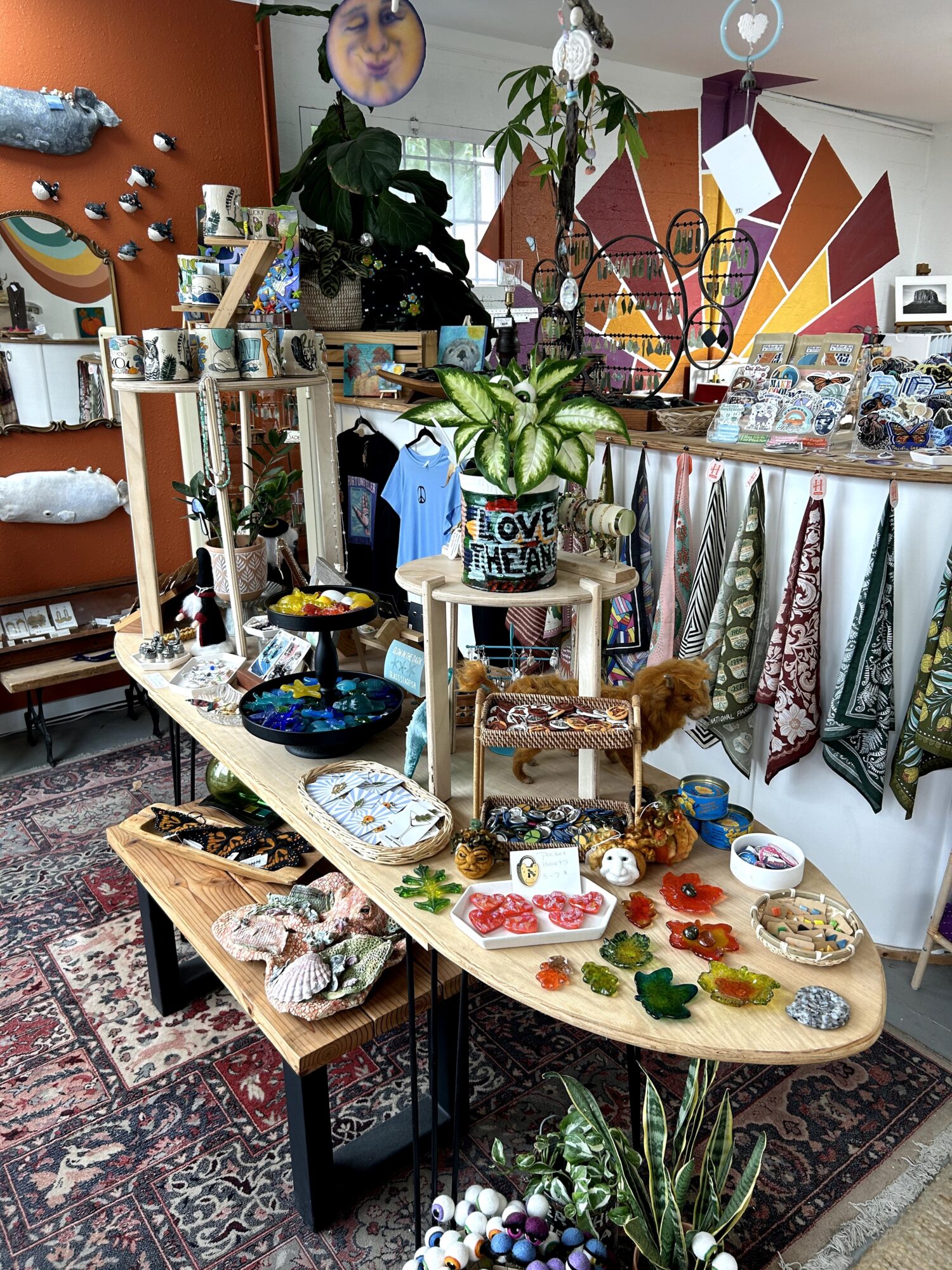 Display table with jewelry, plants, and decorative items in a room with colorful wall art and hanging decorations.
