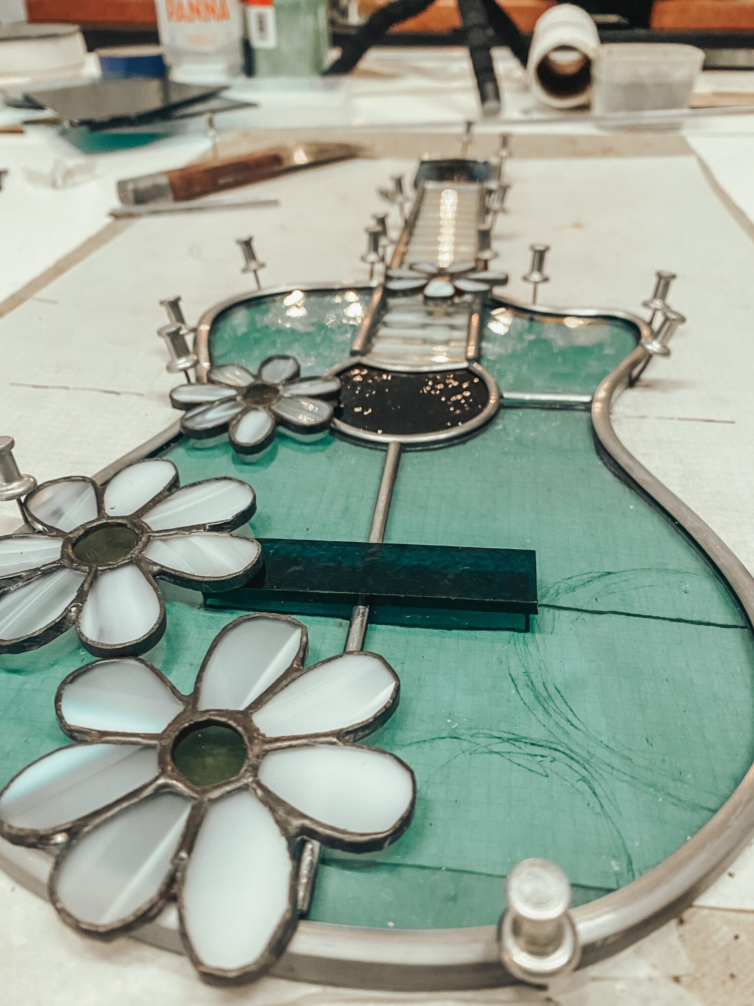 Stained glass window with floral design, metal framework, and green glass background, on a worktable.