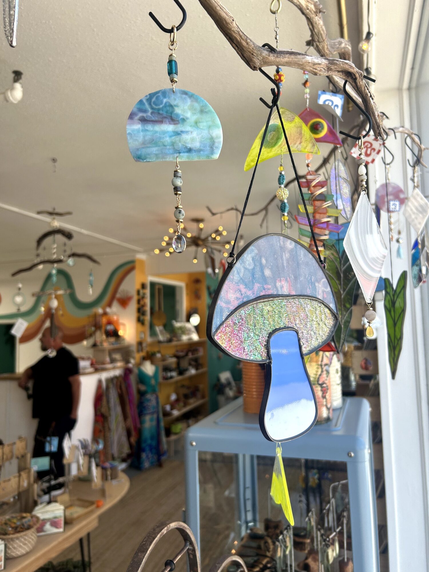 Decorative hanging ornaments made of glass and metal, with a store interior in the background, including clothing displays and a person shopping.