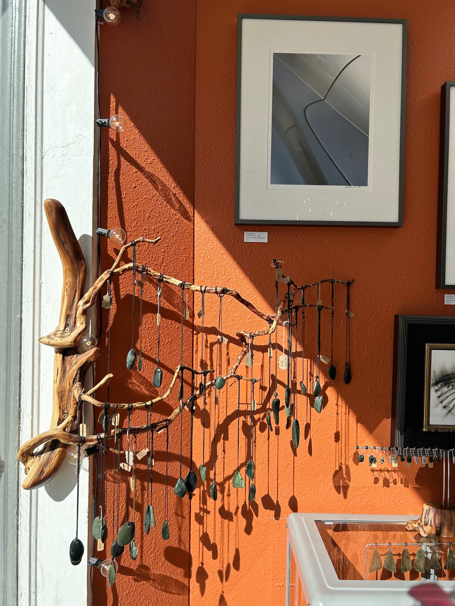 Decorative wall with framed artwork, a driftwood piece, and hanging ornaments casting shadows, next to a sink.
