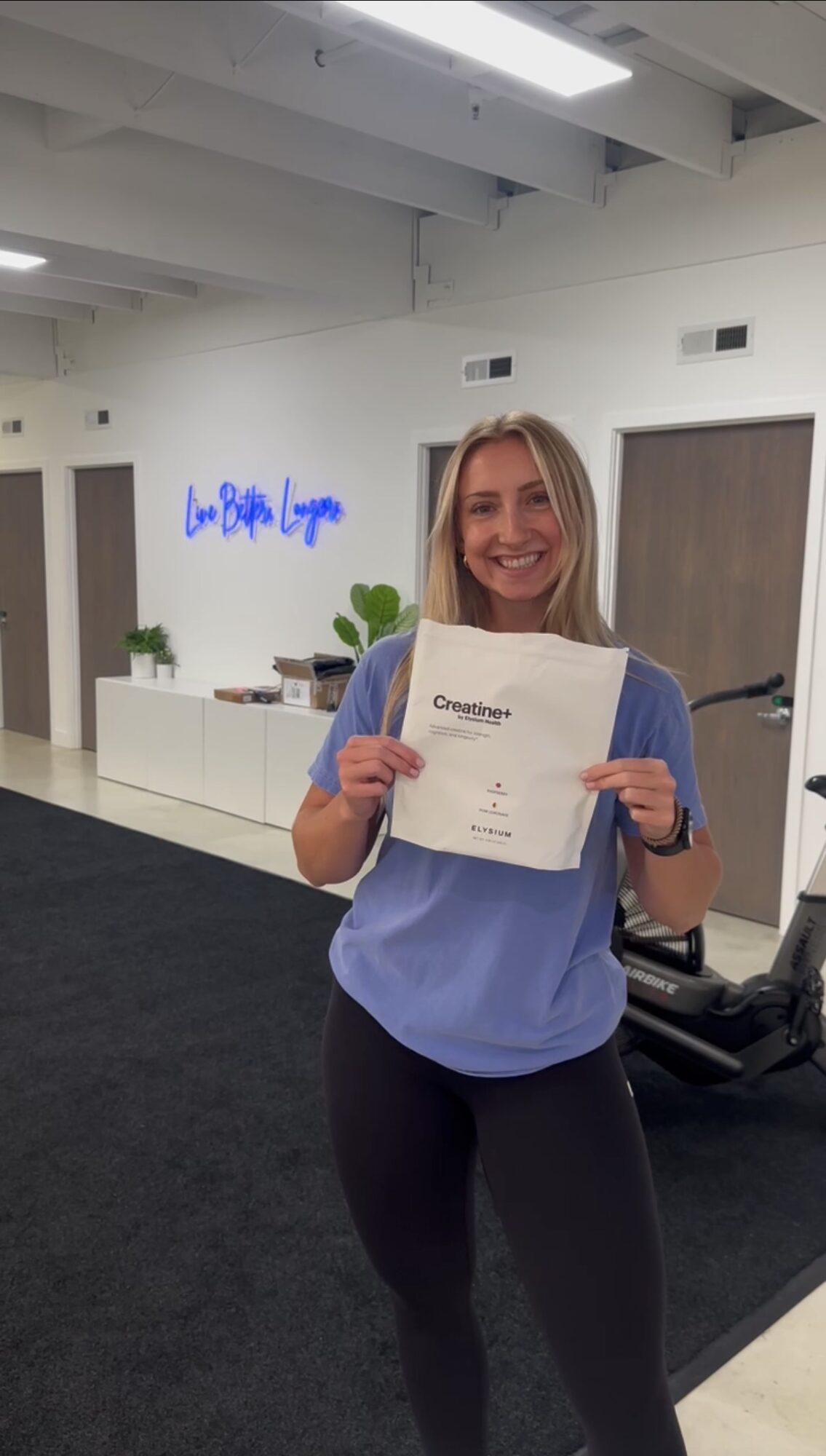 Woman holding a certificate, smiling, standing indoors with white walls and a door in the background.