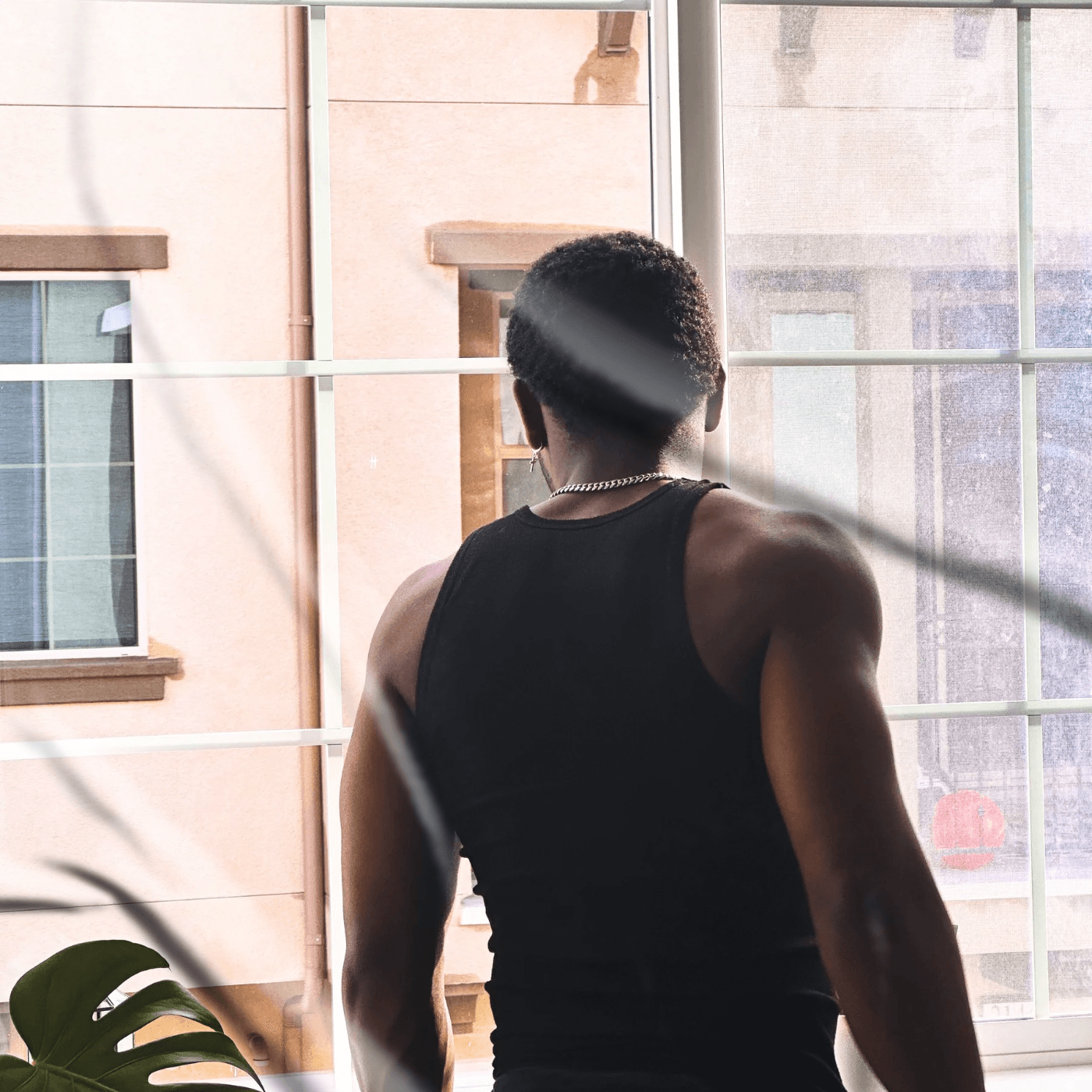 Person with short hair wearing a sleeveless top, facing a window with grid panes, sunlight streaming in.
