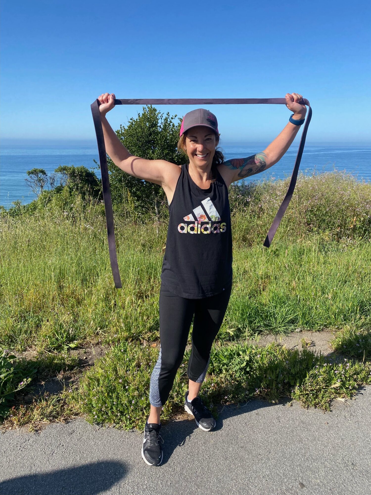 Person standing outdoors holding resistance bands, with a landscape of grass, trees, and water in the background.