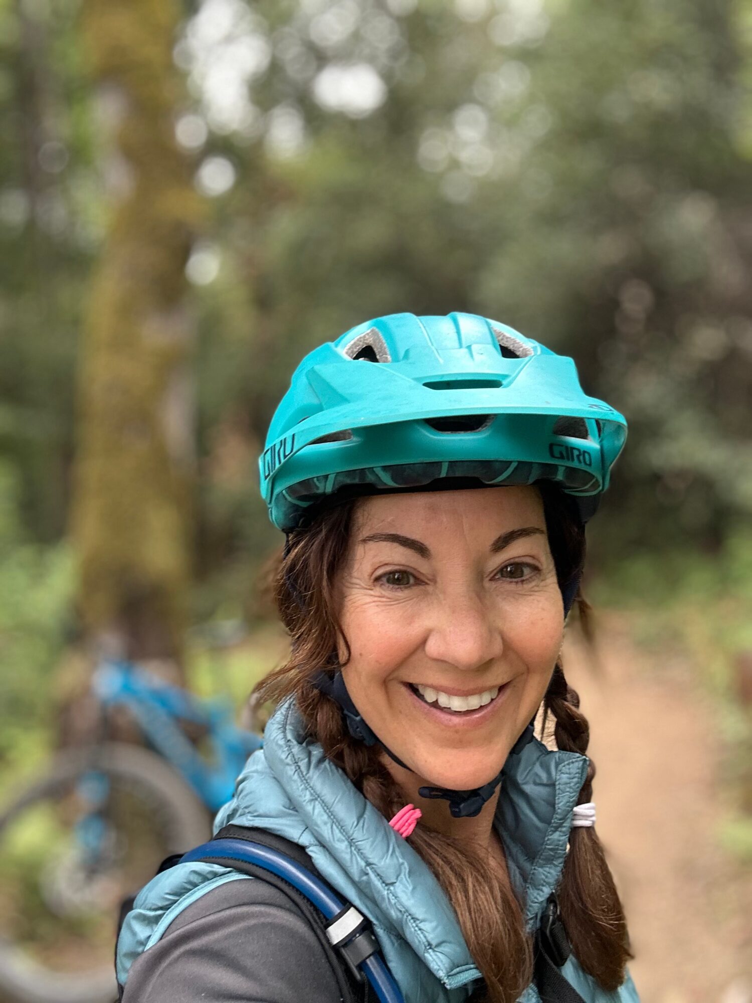 Woman wearing a blue helmet outdoors, smiling, with trees in the background.