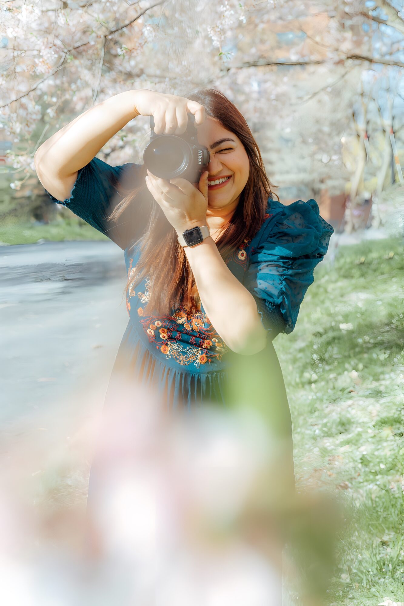 Woman smiling outdoors, holding a balloon, with trees and grass in background.