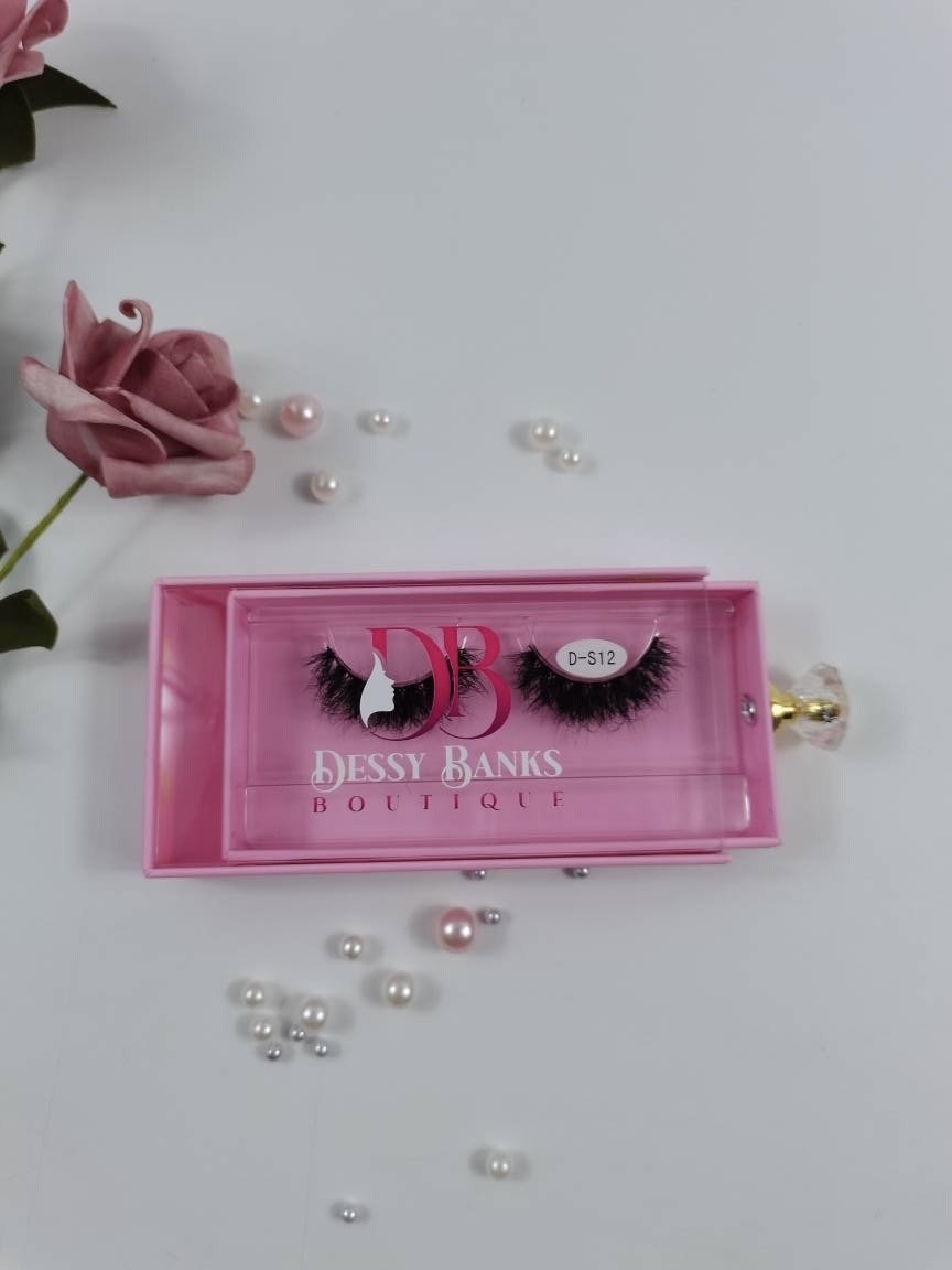 Pink box with false eyelashes and pearls scattered around, pink flower in top left corner, on a white background.