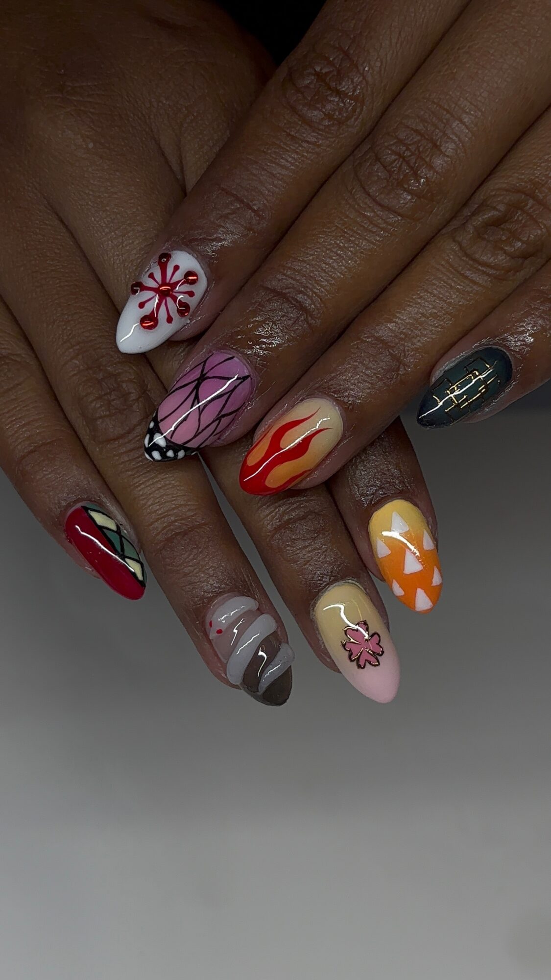Close-up of hands with colorful, decorated nail art on each fingernail, featuring various patterns and designs.