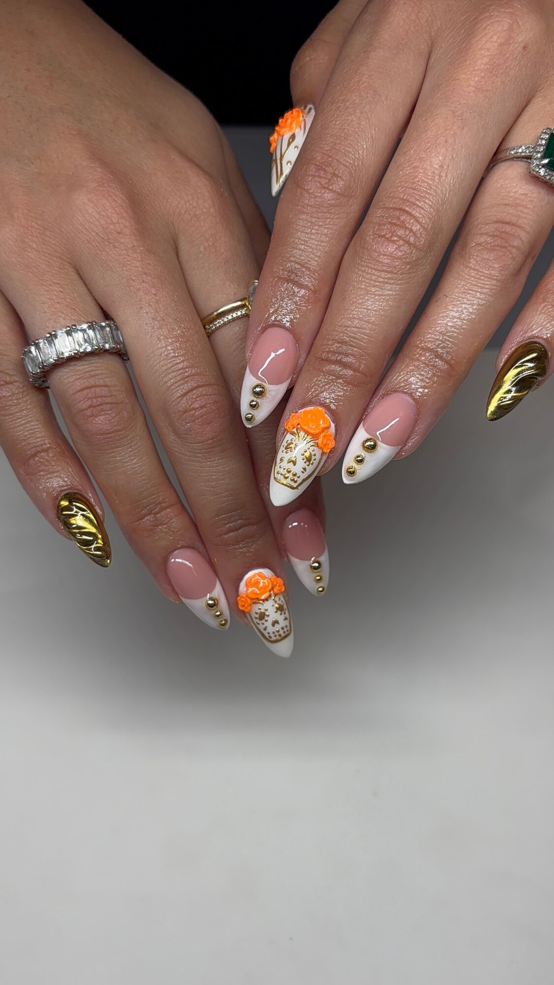 Two hands with decorated nails, rings, and a gold accent nail, resting on a surface.