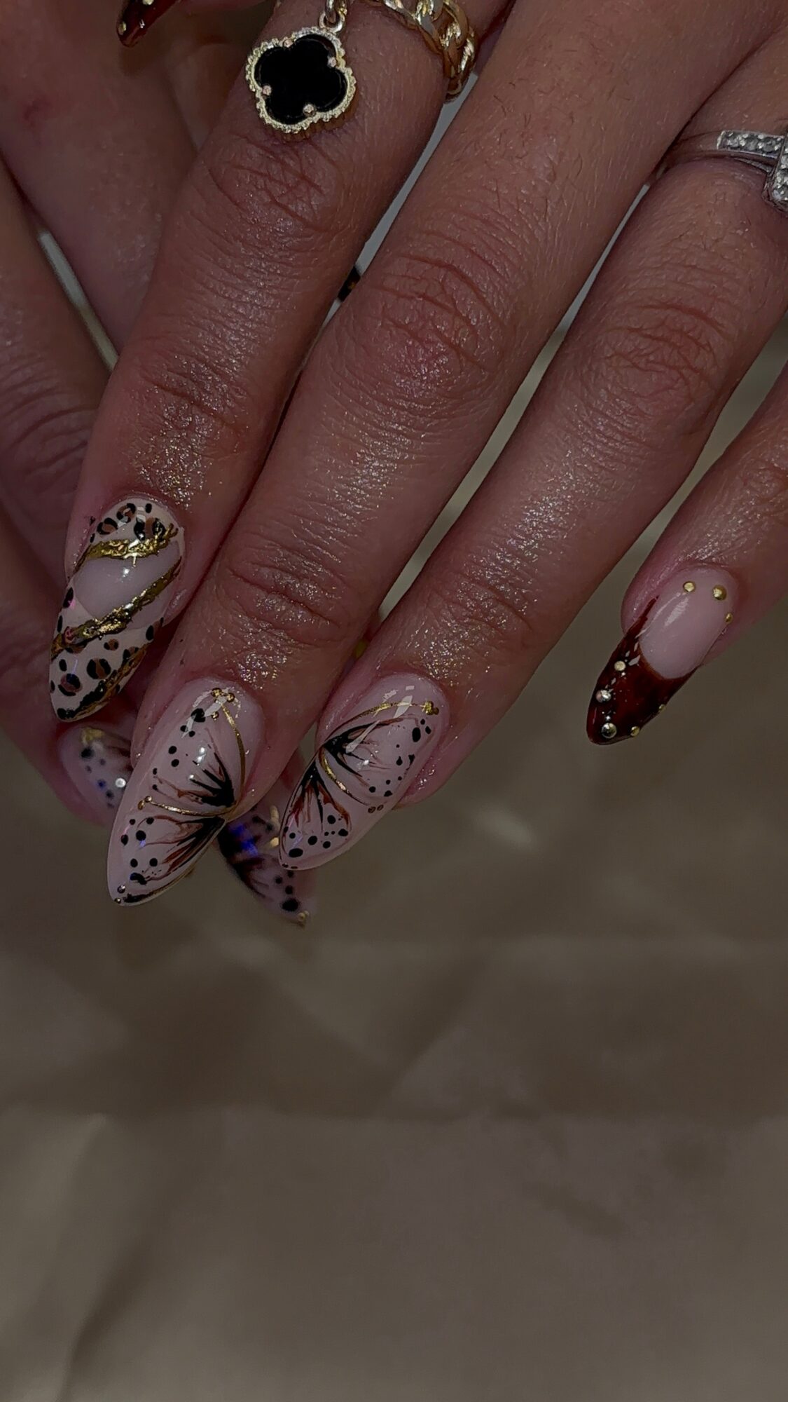 Close-up of hands with decorated nails featuring floral and abstract designs, rings, and jewelry, against a neutral background.