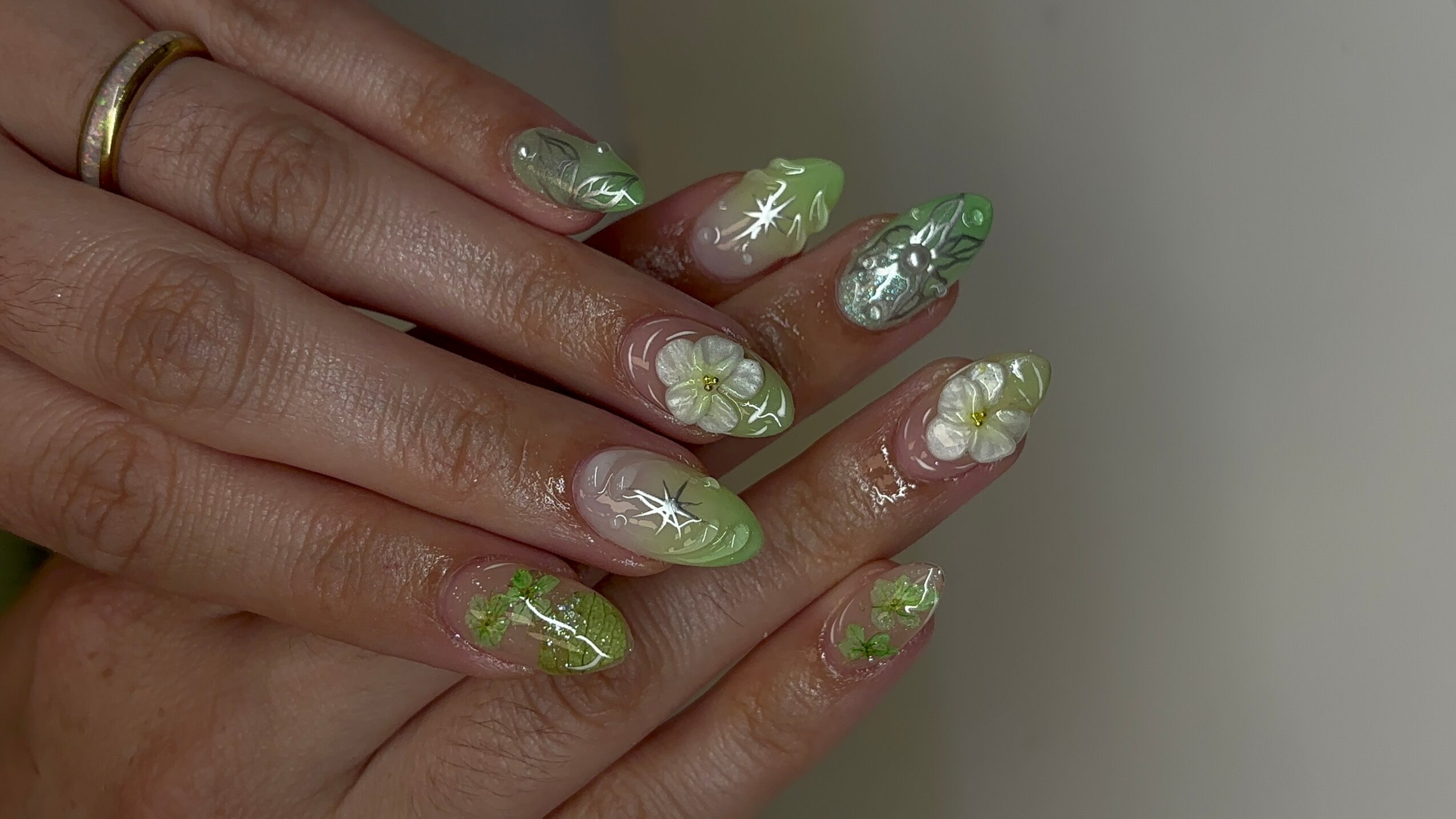 Close-up of hands with decorated nails featuring green, white, and silver designs, including stars and floral patterns.