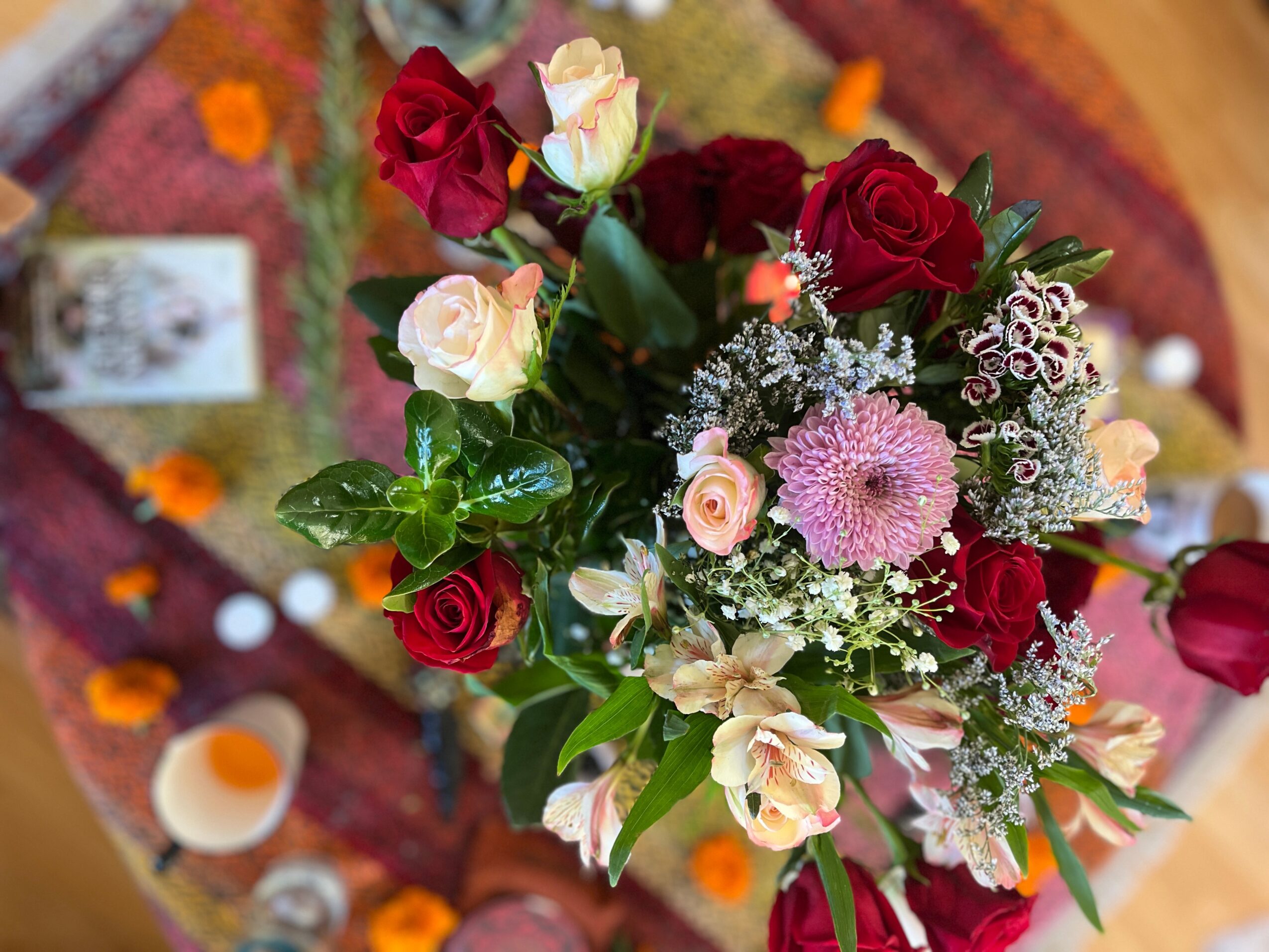 A bouquet of red, white, and pink roses with baby's breath on a table with drinks and flowers