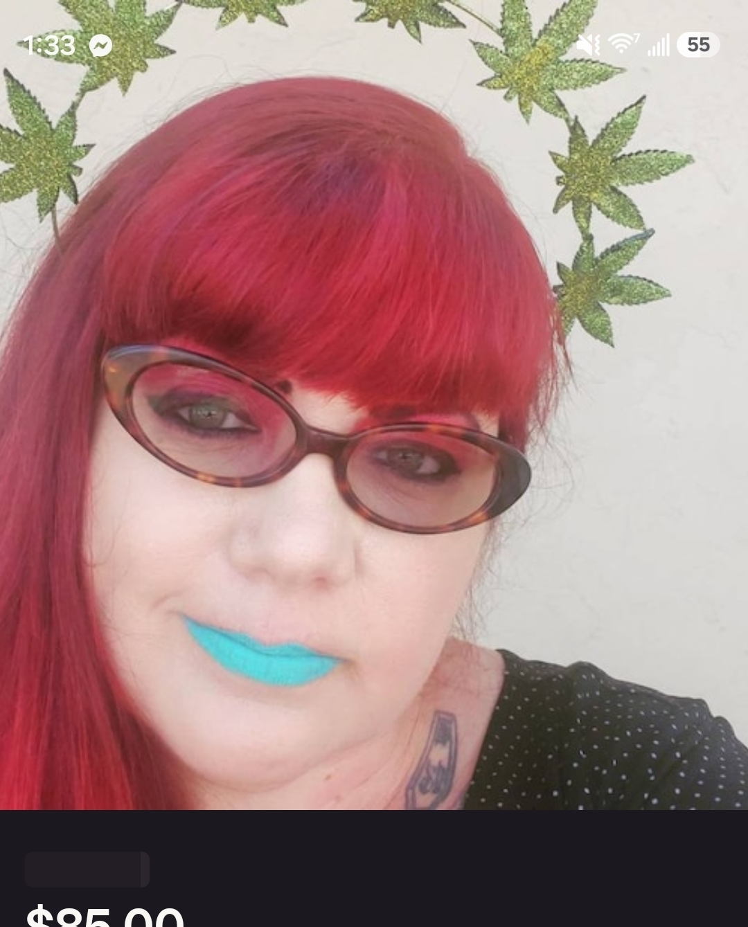 Person with red hair, wearing glasses, blue lipstick, and a black top, with green leaf decorations in the background.