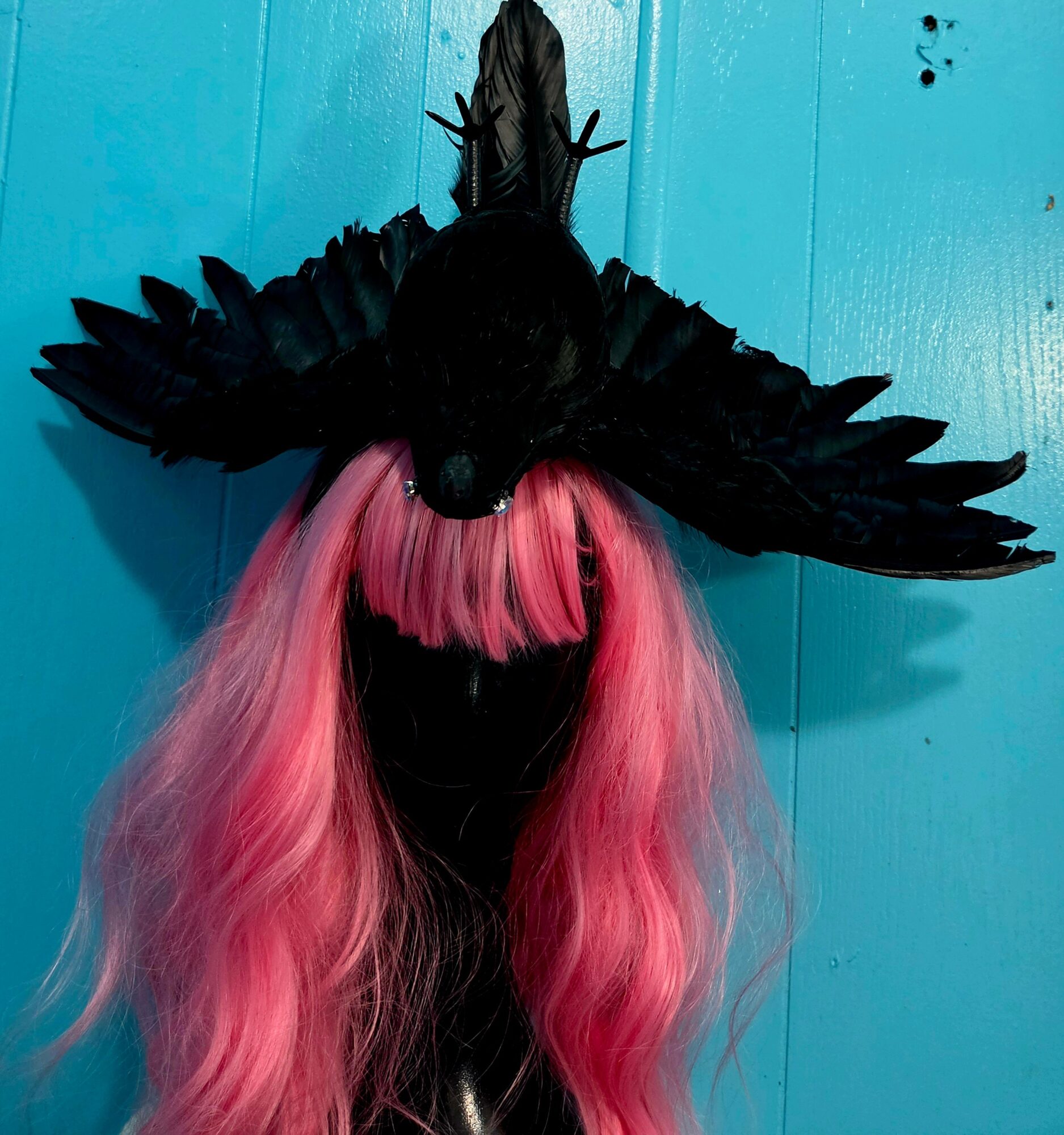 Person wearing a black bird mask with pink hair, against a blue background.